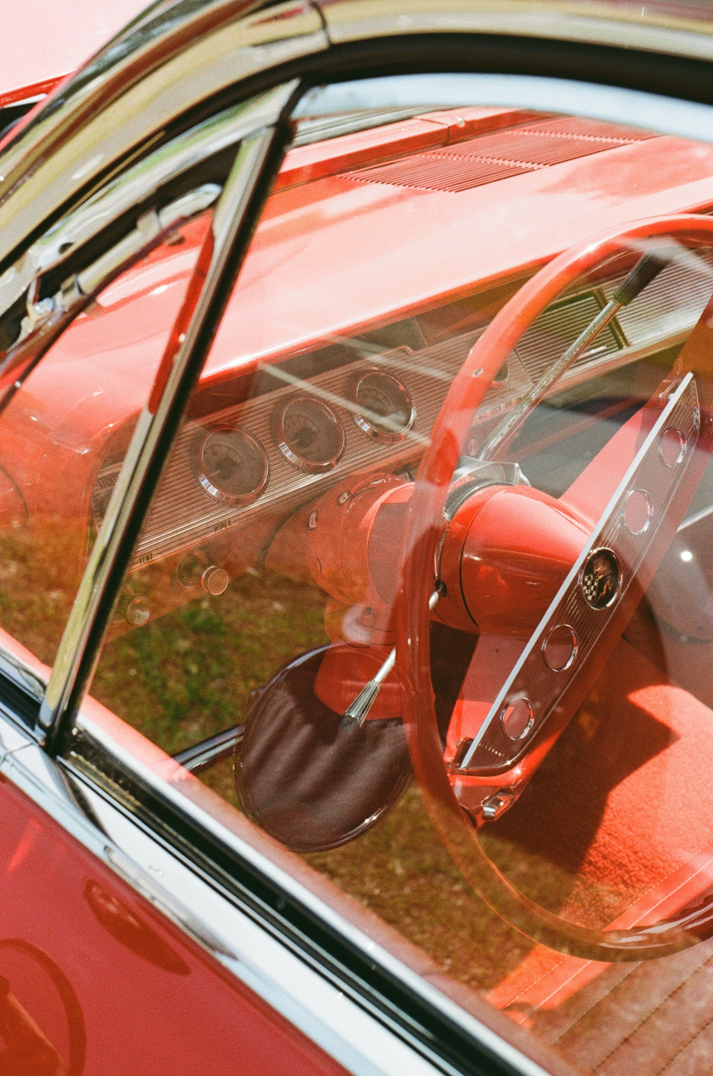 Close-up of vintage red car dashboard and steering wheel seen through side window.