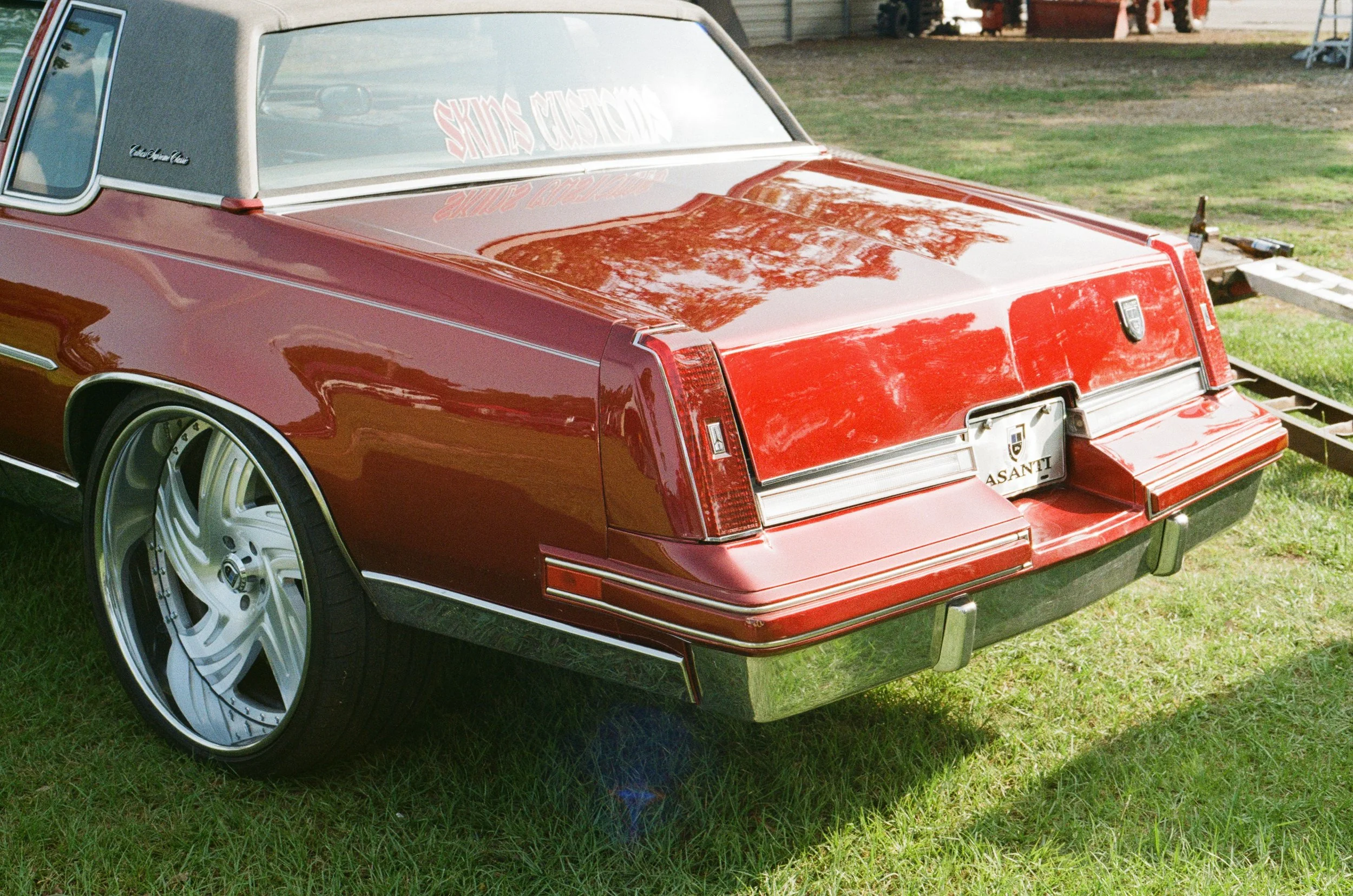 Red vintage Cadillac car parked on grass with custom window decal and shiny wheels.