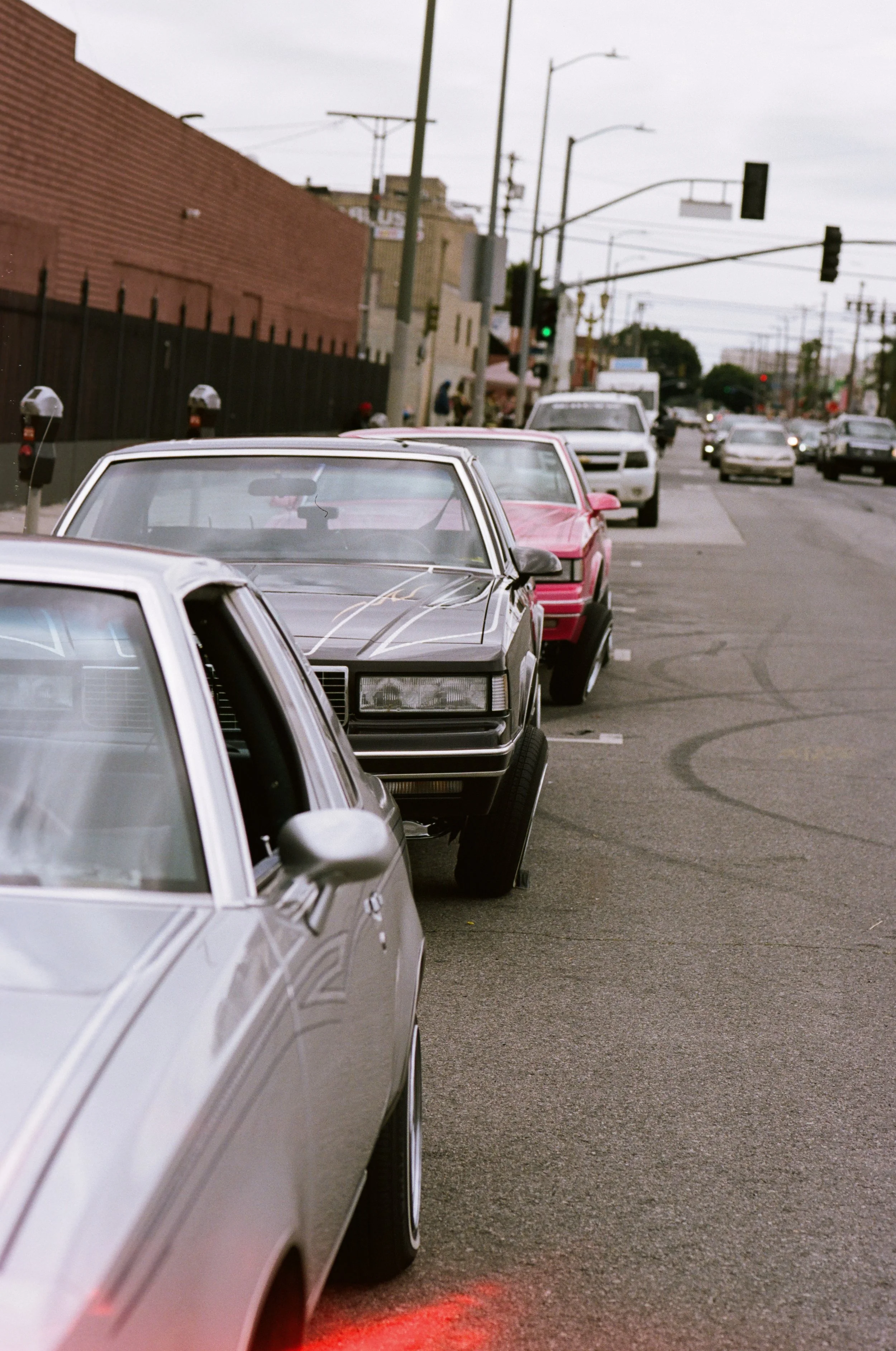 Street view showing cars parked along the sidewalk and traffic signal in the background on an overcast day.