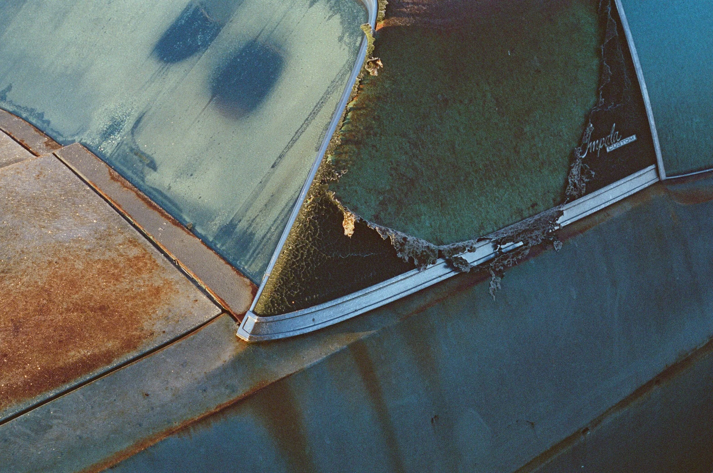 A close-up view of a broken and damaged window with mold and dirt around the edges, situated at the corner of a building or structure.