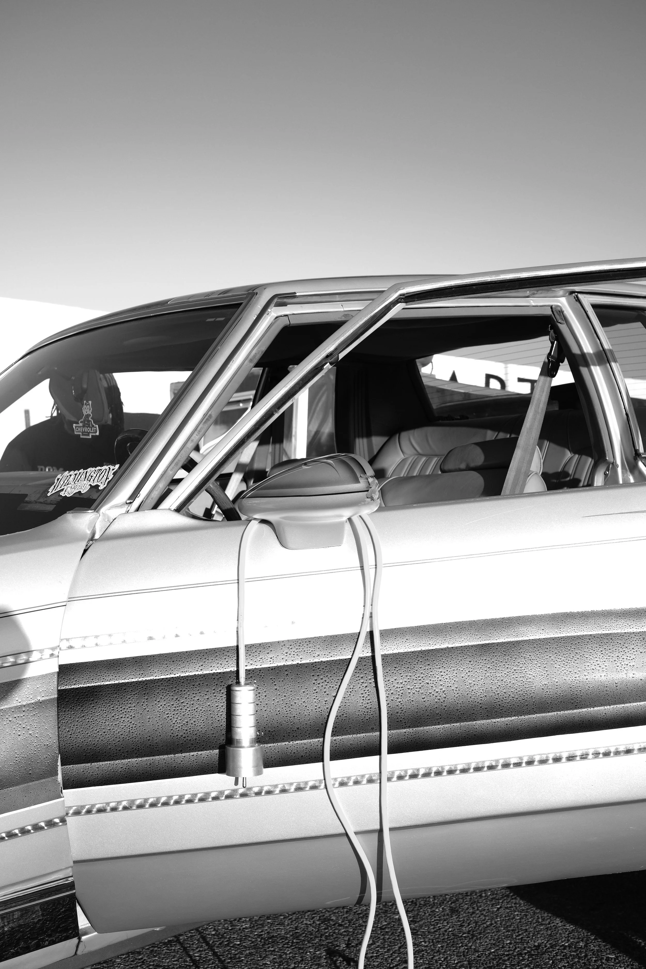 Black and white photo of an electric car charging at a charging station, with a charging cable connected to the vehicle.