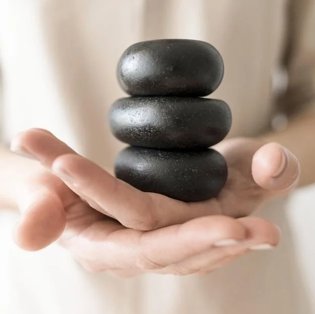 Four smooth, black stones balanced on a person's open hand.
