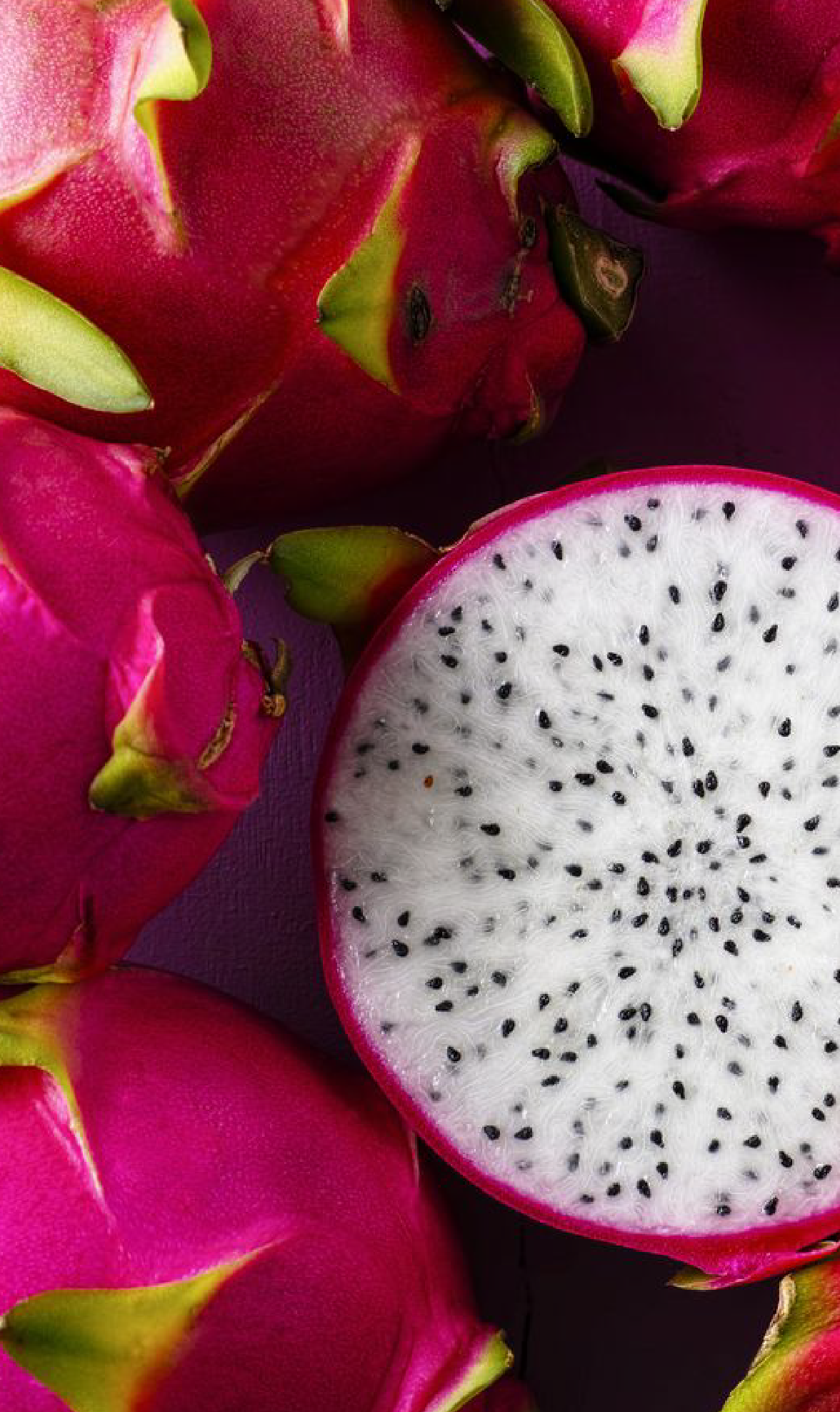 Close-up of a halved dragon fruit with white flesh and black seeds, surrounded by whole pink and green dragon fruits.