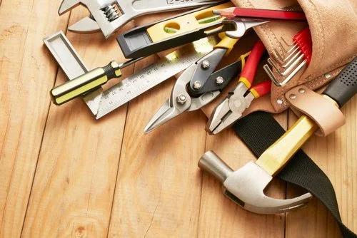 Assorted hand tools on a wooden workbench, including a hammer, pliers, a level, a wrench, a screwdriver, and a measuring tape in a tool bag.