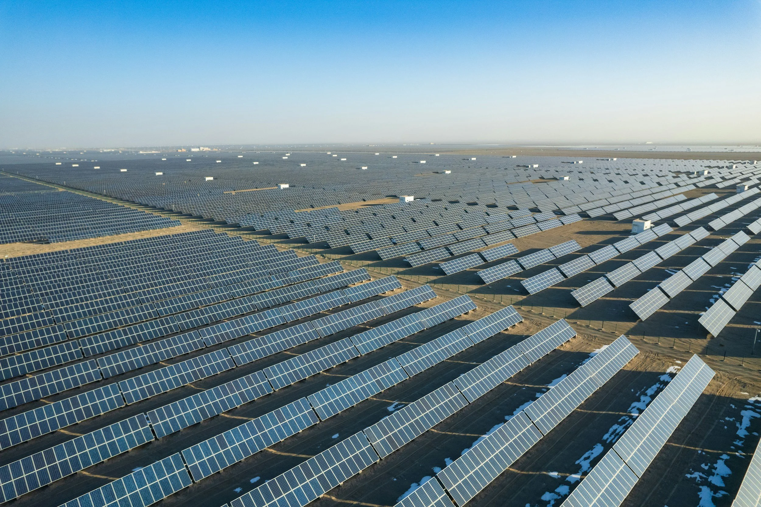 A large solar panel farm with rows of solar panels extending into the distance under a clear blue sky.