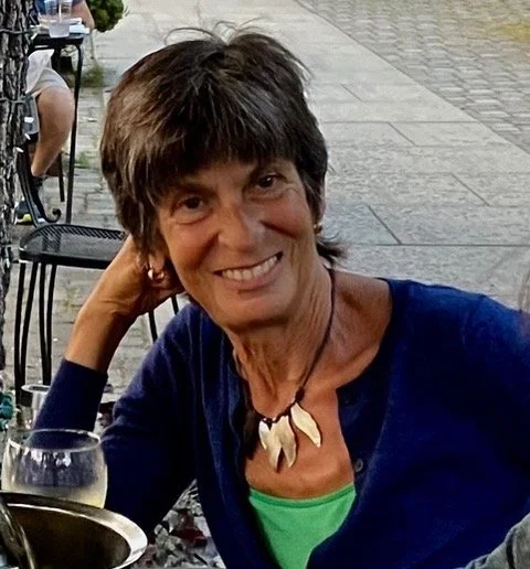 A woman with short brown hair smiling at an outdoor restaurant or cafe.
