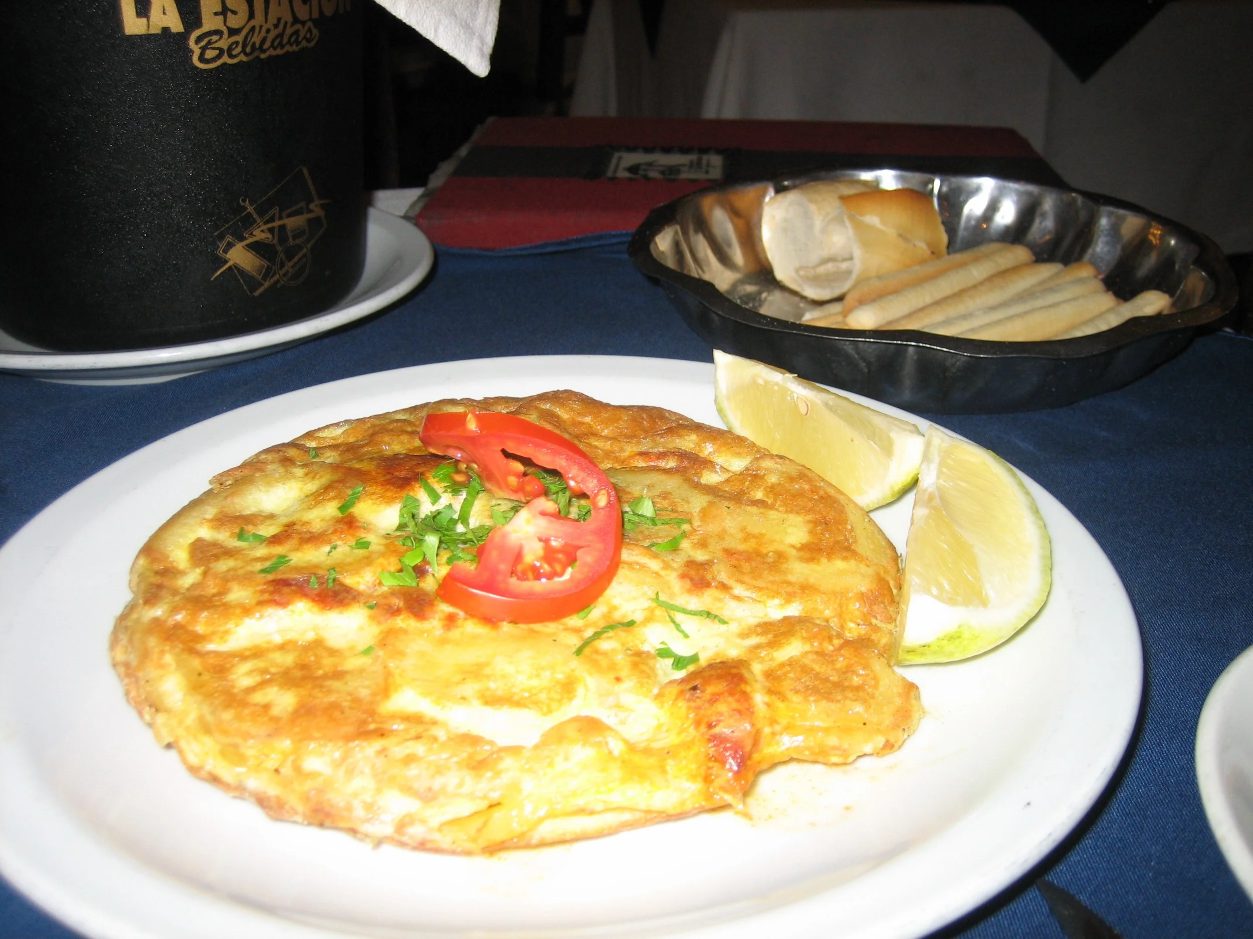 A plate with a cooked omelette garnished with tomato slices and chopped green herbs, served with lemon wedges.