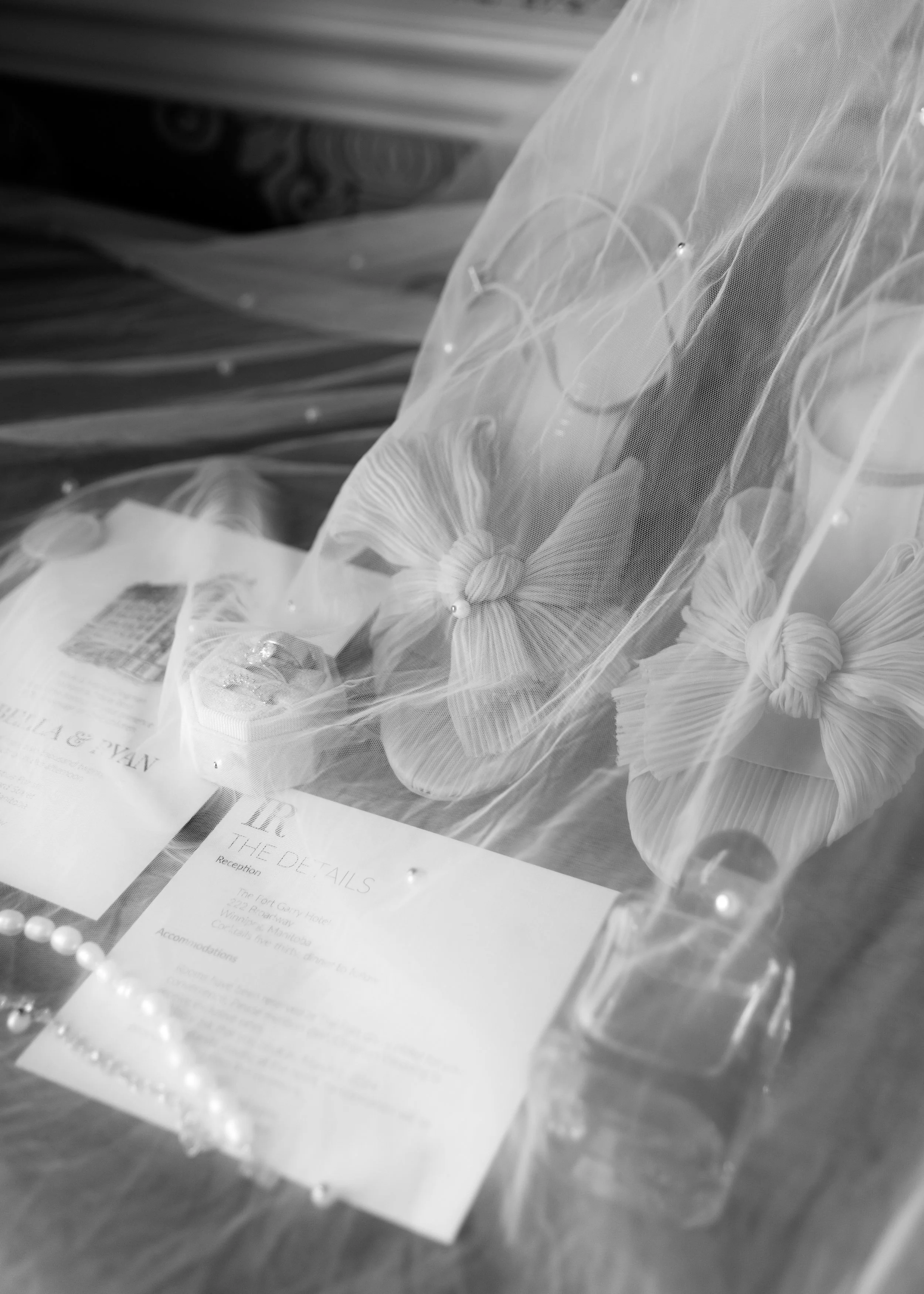 Velluto Events Co. Wedding A wedding keepsake display with tied wedding dress bows, pearl jewelry, a wedding invitation, and decorative pearls on a table.