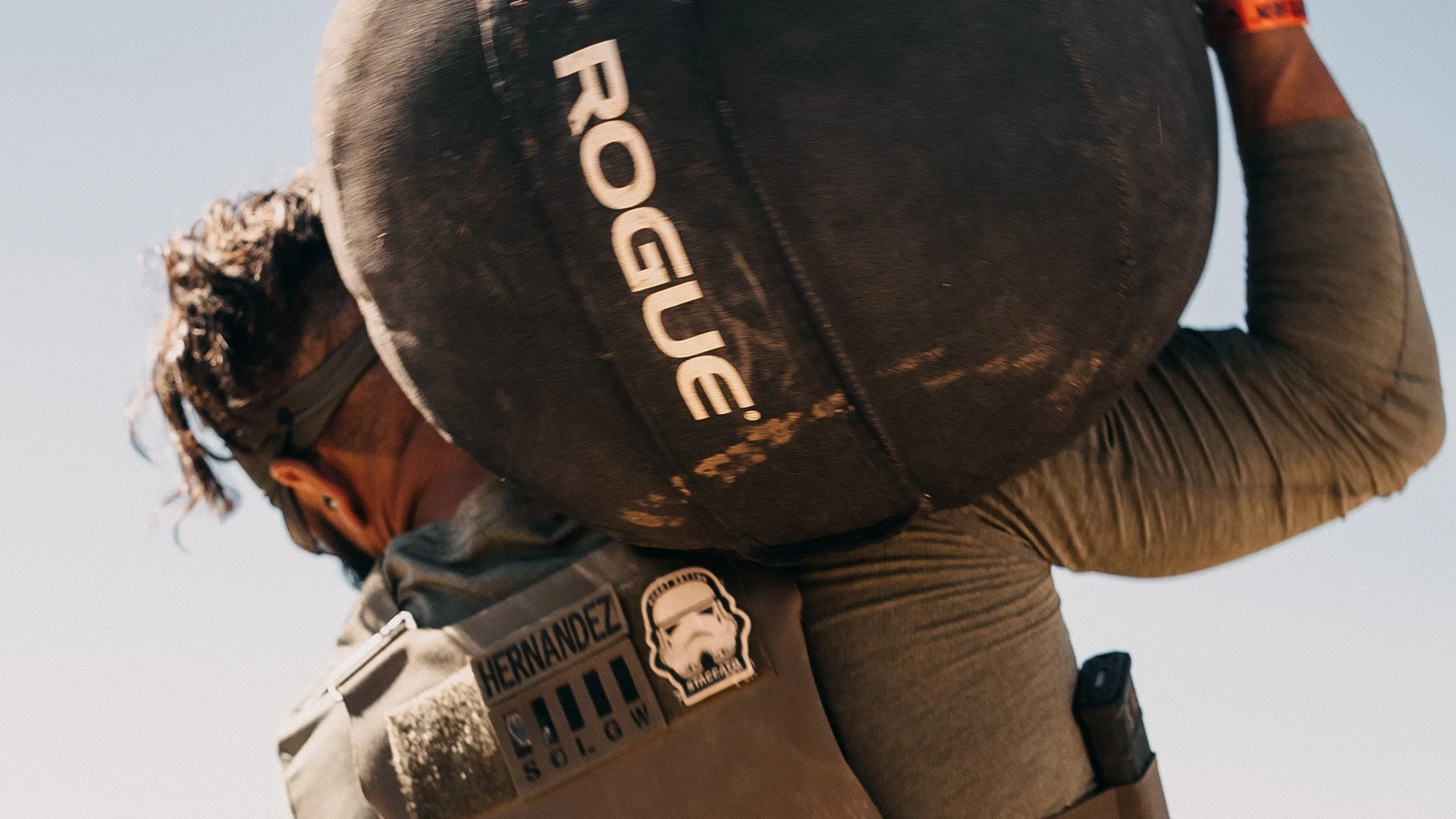 A person wearing sunglasses and a Star Wars Stormtrooper patch on a tactical vest, carrying a large bag with 'ROGUE' written on it, outdoors against a clear sky.
