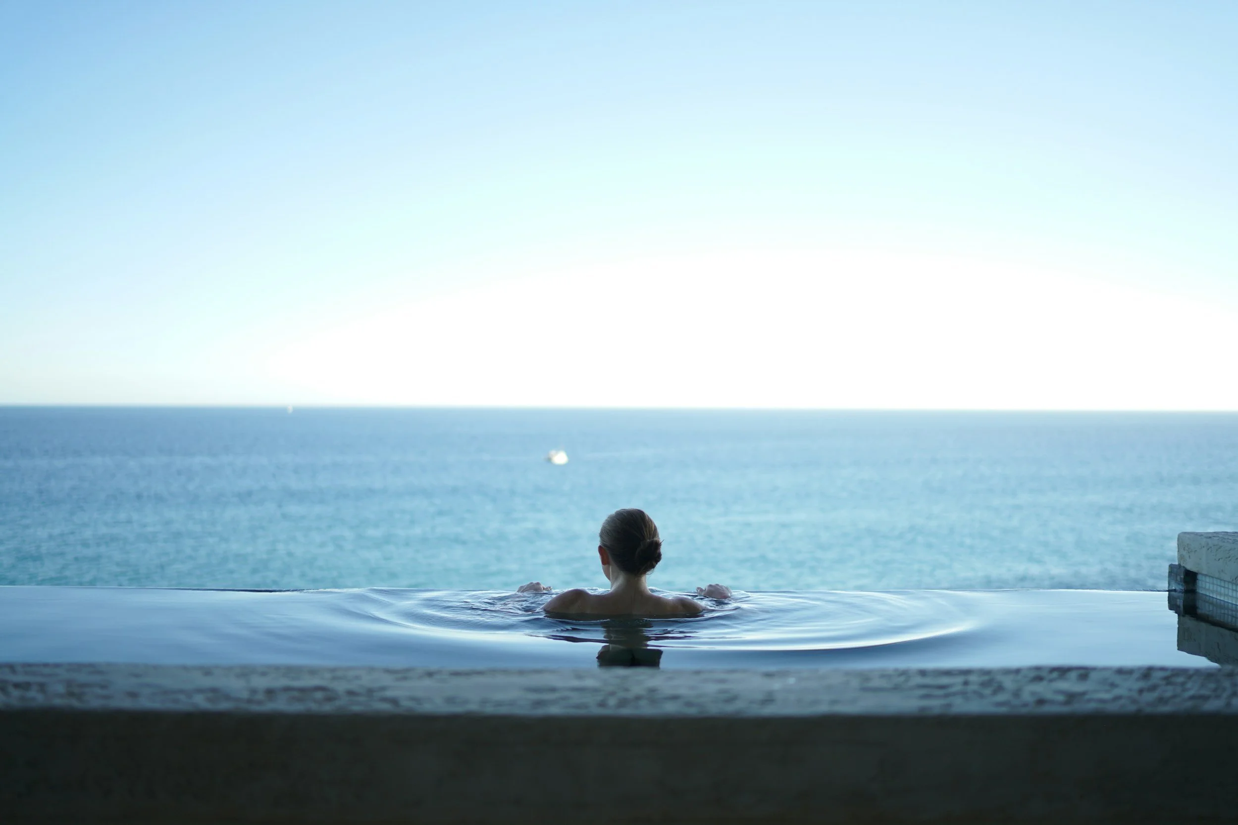 A person relaxing in an infinity pool overlooking the ocean.