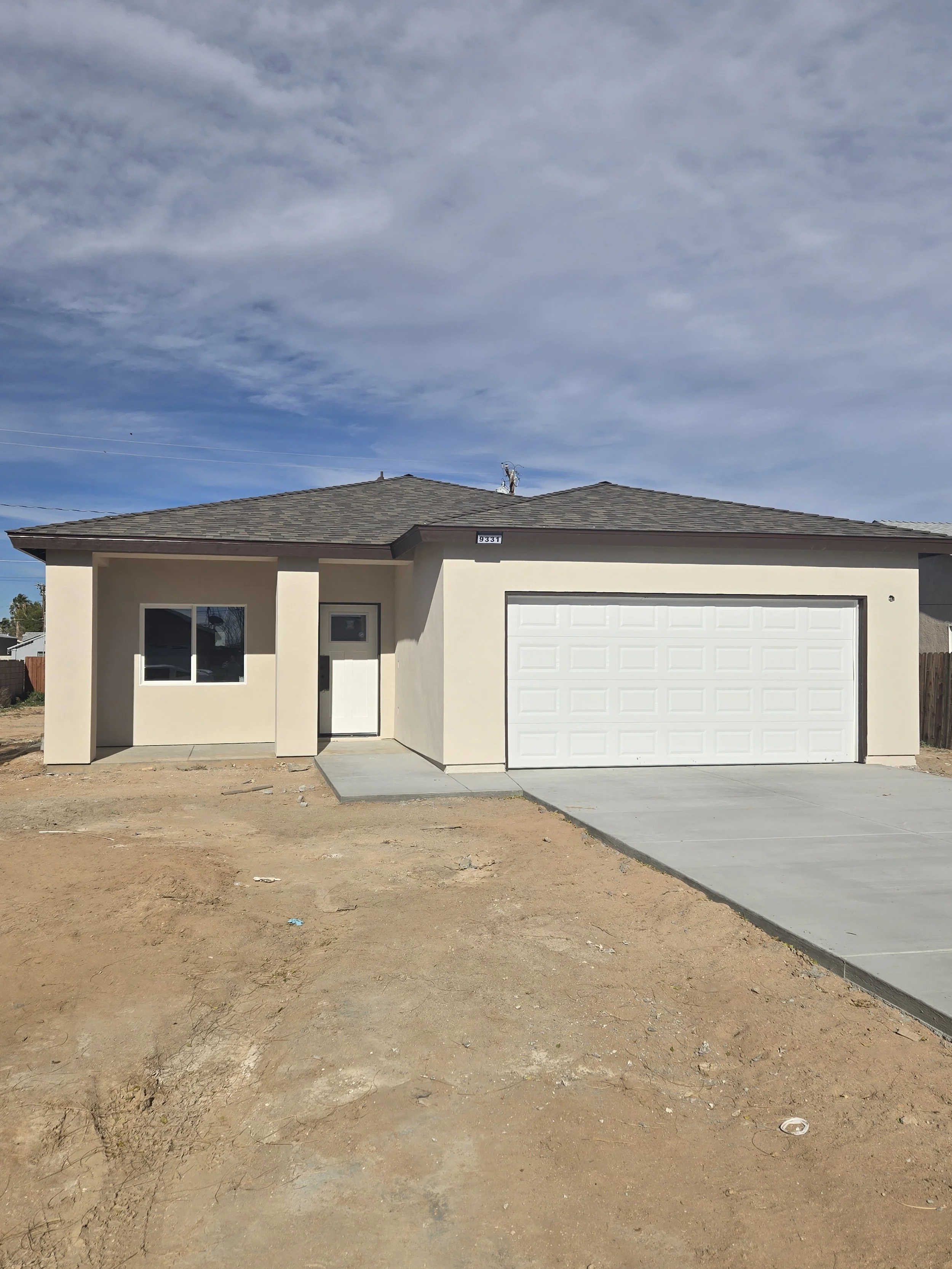 Newly built single-story house with a two-car garage, a front door, and a window, under a partly cloudy sky.