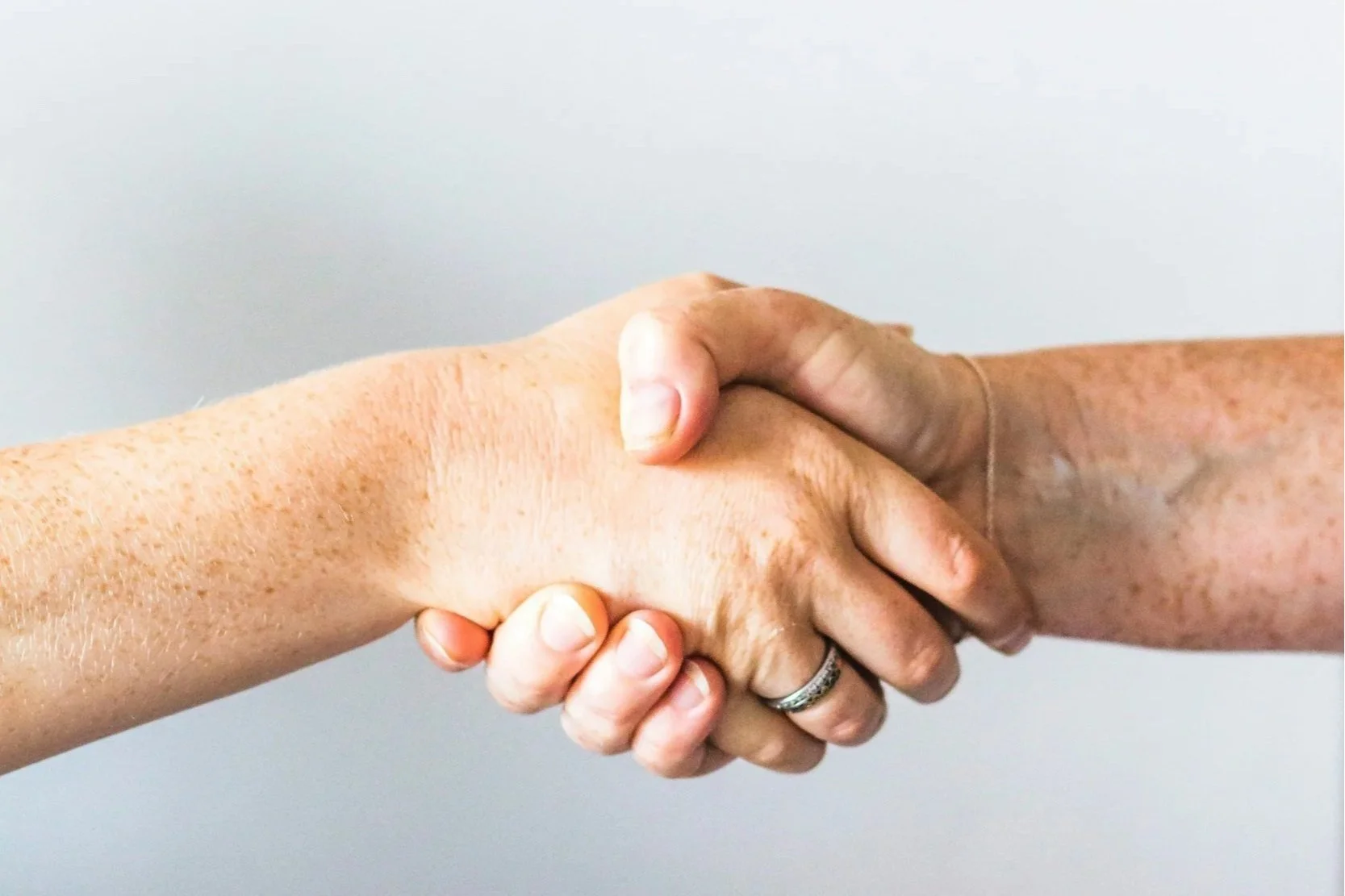 Close-up of two hands gripping each other in a handshake against a plain background.