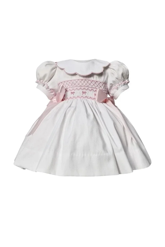 A white and pink baby dress with puffed sleeves, a scalloped collar, and smocked embroidery on the bodice.
