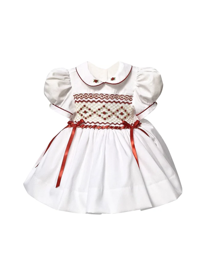White dress for a young girl with puffed sleeves, embroidered details, a Peter Pan collar with red trim, and red ribbon accents.