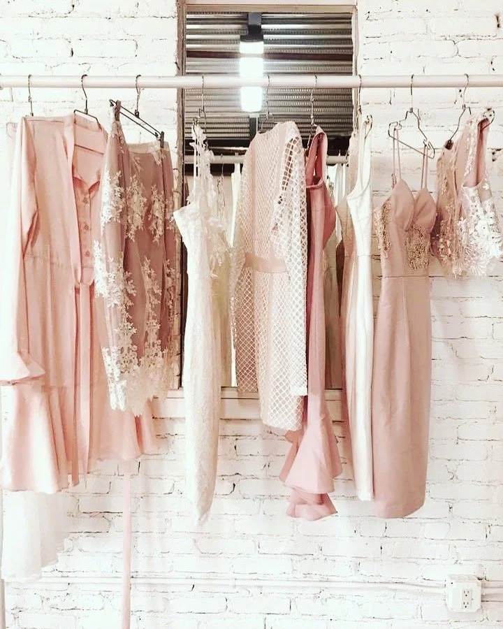 A row of pink and white dresses hanging on a clothing rack against a white brick wall.