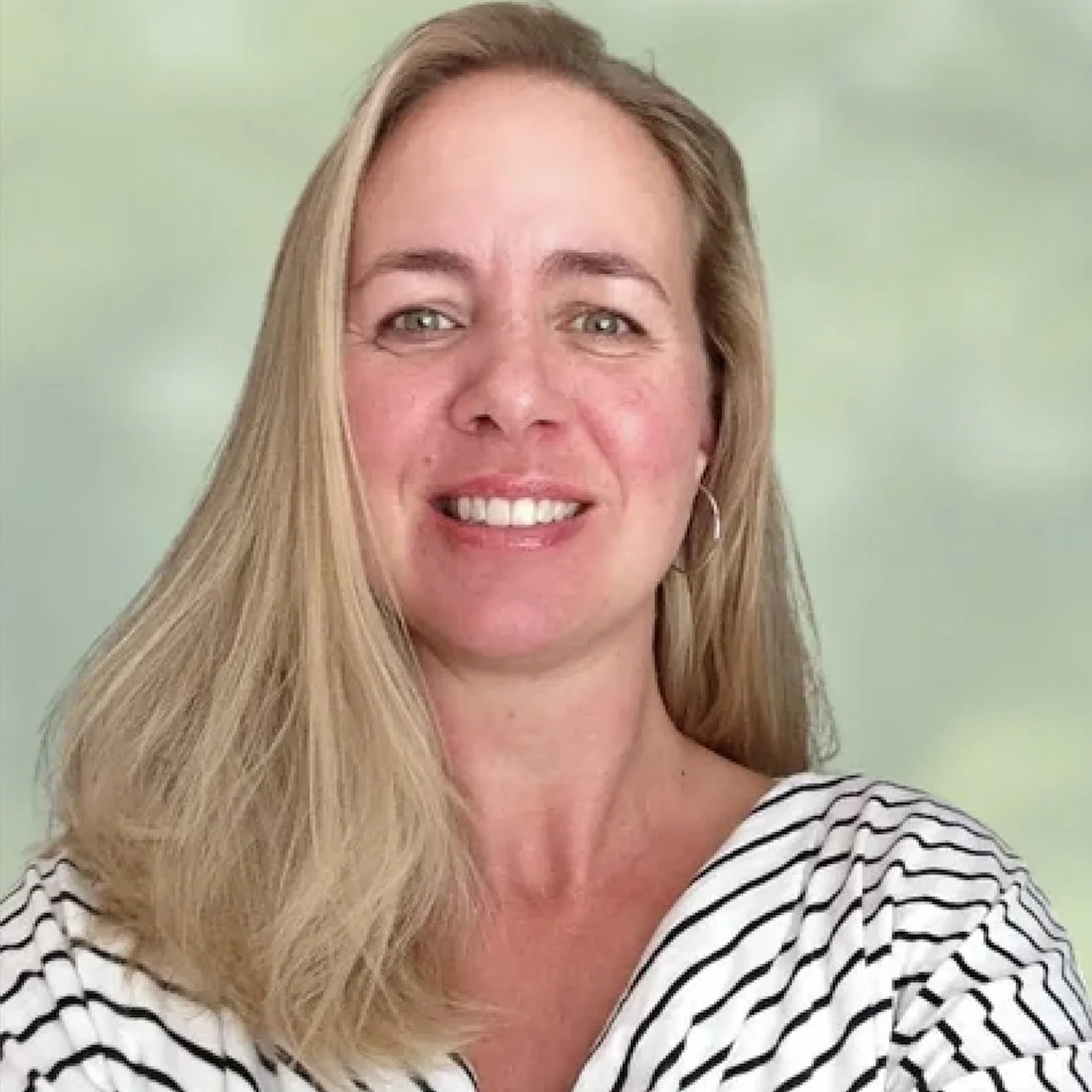 A woman with long blonde hair, smiling, wearing a white and navy striped shirt, against a light green background.