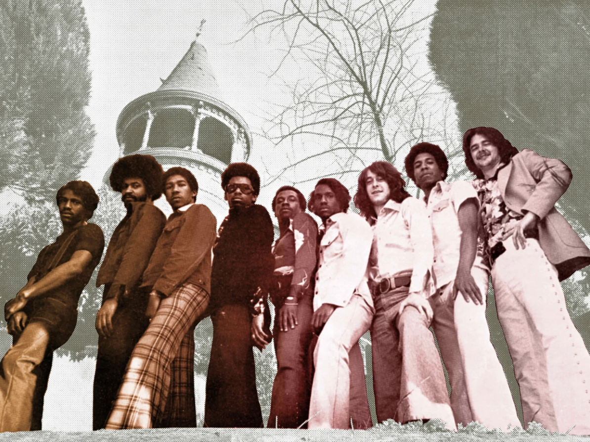 Vintage black and white photo of a group of men standing outdoors in front of a tower and leafless trees, with some colorized elements.