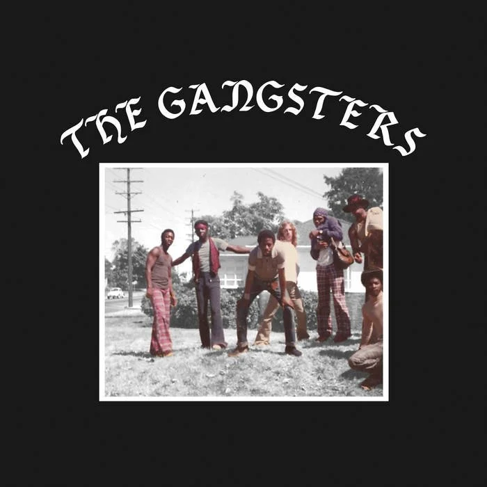 An old black-and-white photograph of six men with casual clothing outdoors, with a black background and the text 'The Gangsters' above the image.