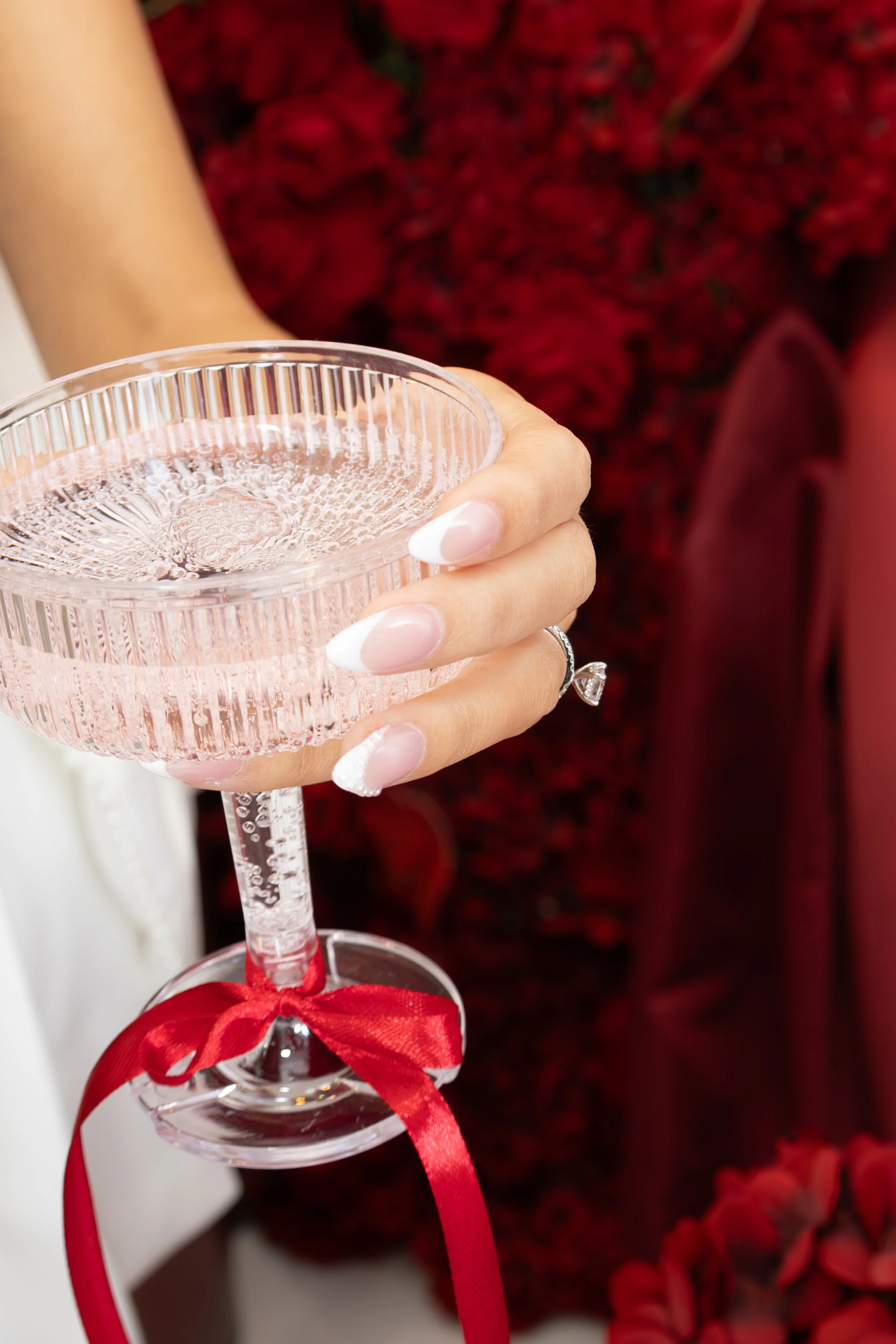 A woman holding a delicate, pink, ribbed champagne glass with a red ribbon tied around the stem.