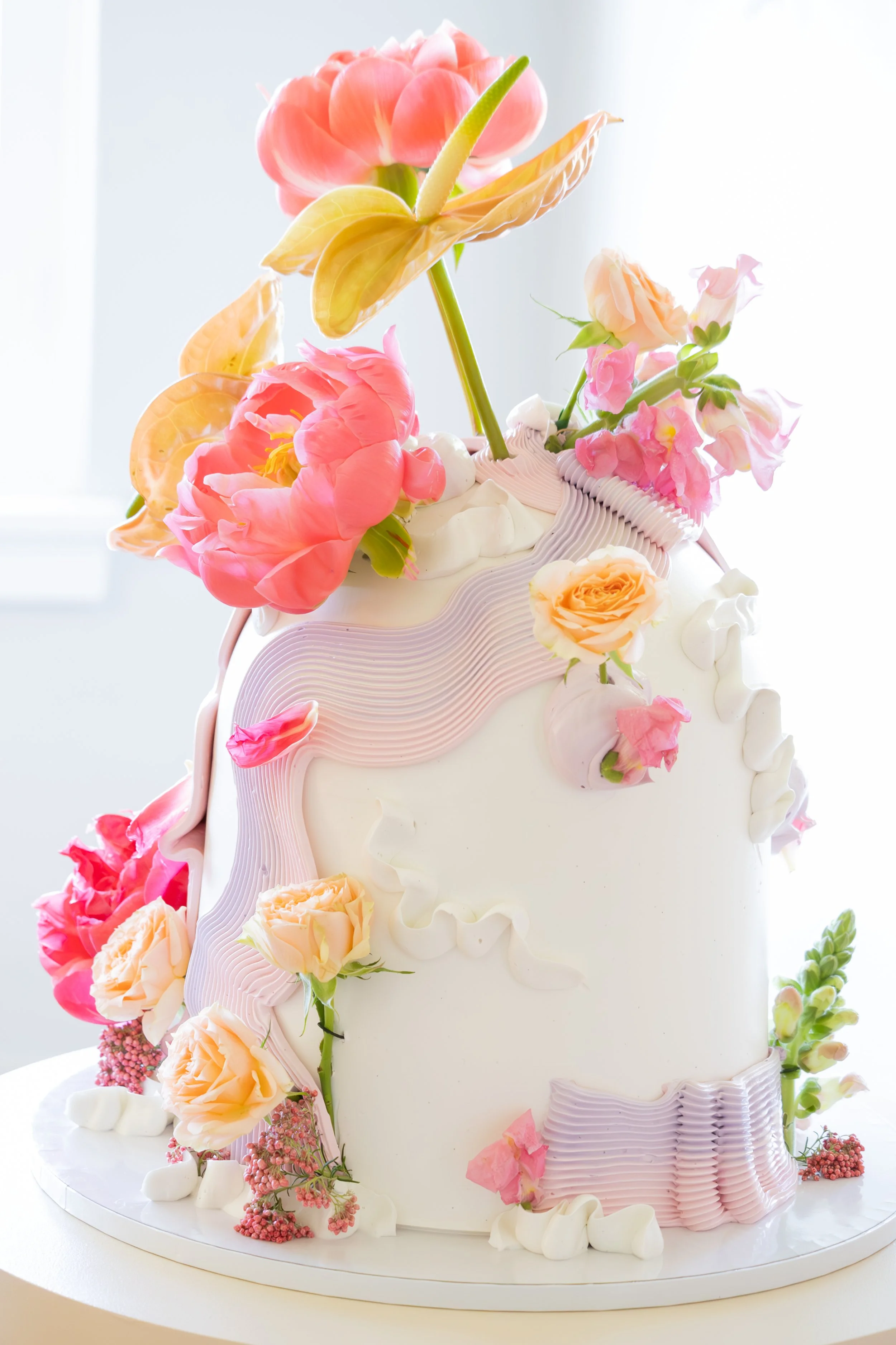 A multi-tiered white wedding cake decorated with pink and peach flowers, ruffled icing, and a floral topper.