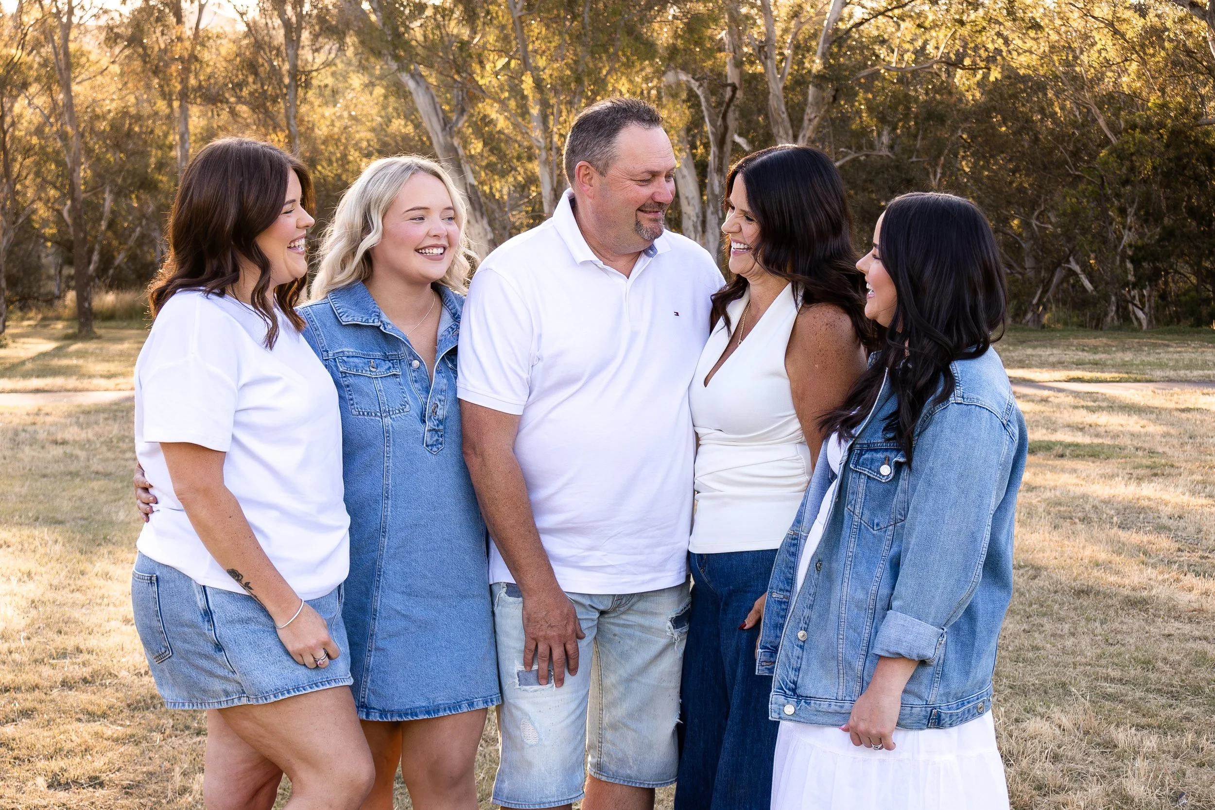 Family gathering outdoors with four women and one man smiling and talking in a park during daytime.