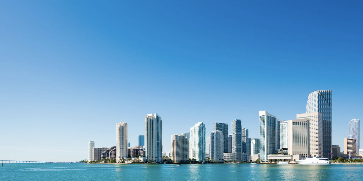 A city skyline with tall modern skyscrapers along the waterfront under a clear blue sky.
