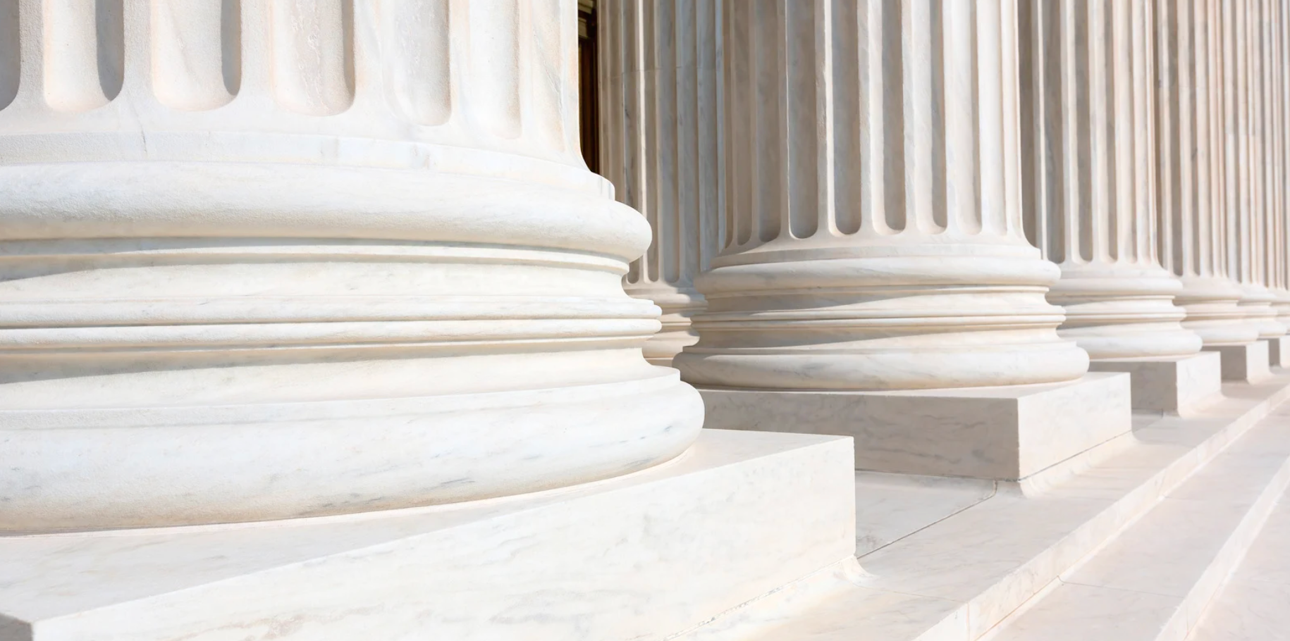 Close-up of marble columns with fluted design and steps in front of them.