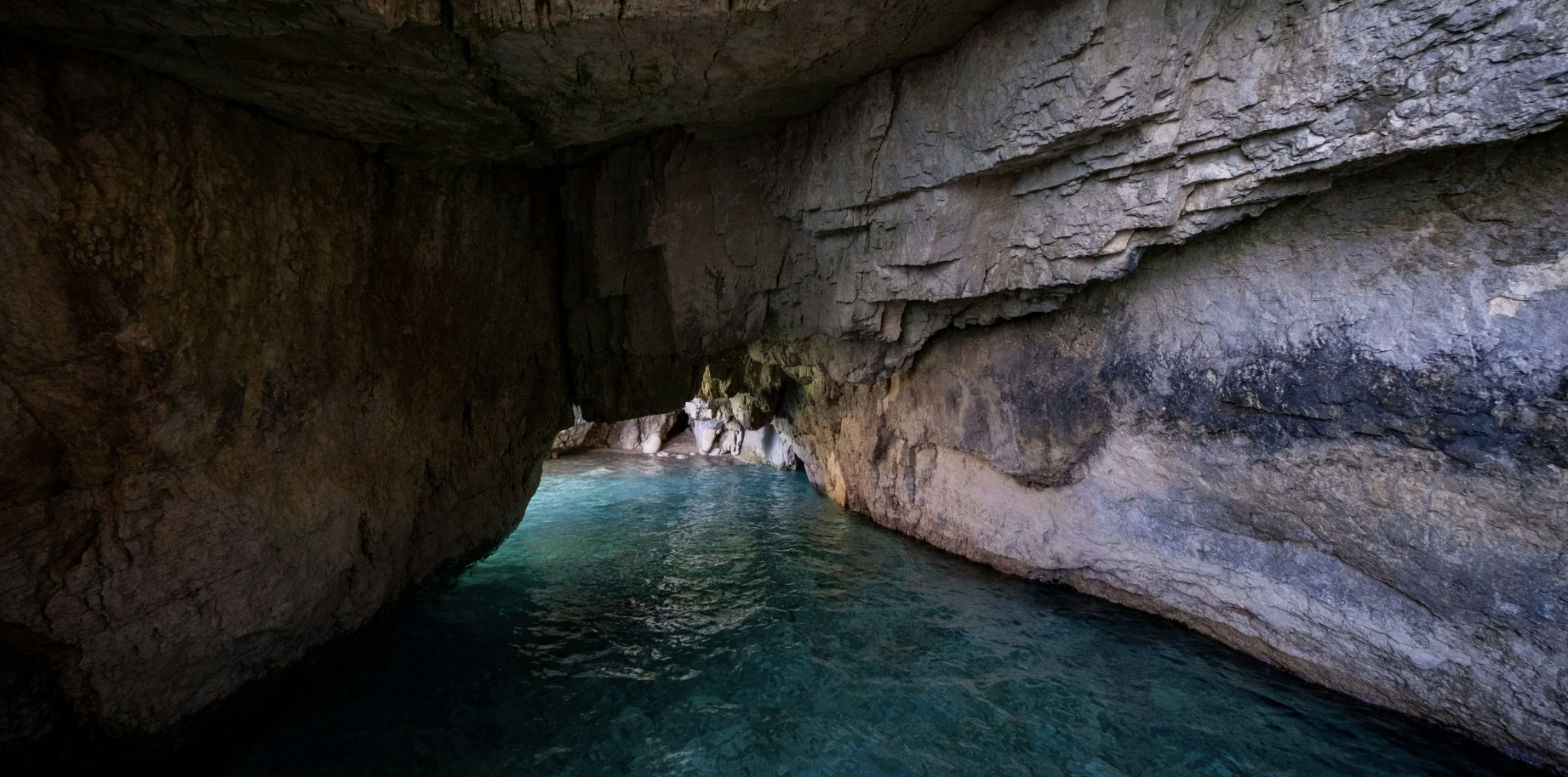 A rocky cave with a small opening revealing turquoise water inside.