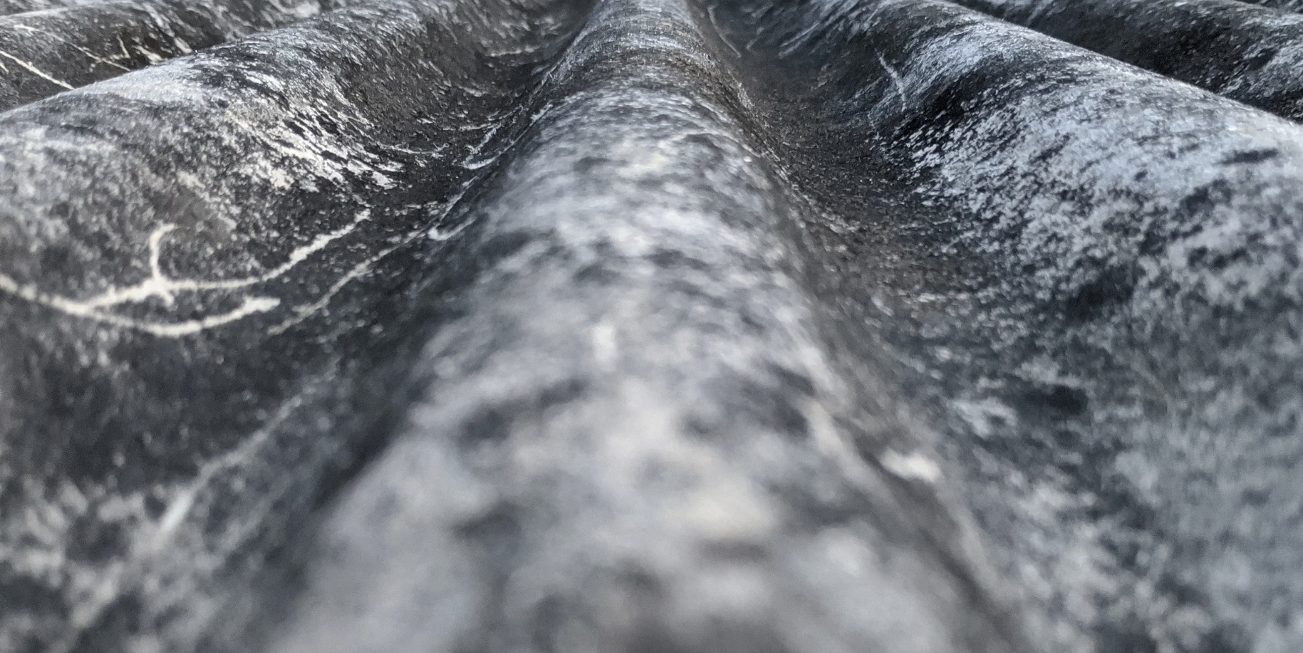 Close-up image of textured black fabric or material with a central seam or fold.