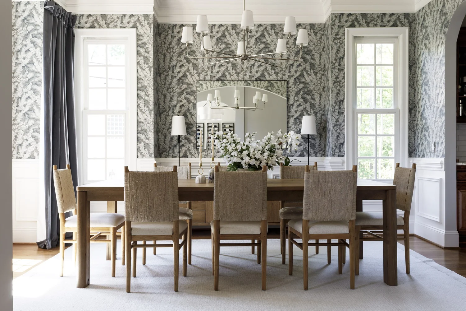 Dining room with fern wallpaper, wood table, woven chairs and white chandelier