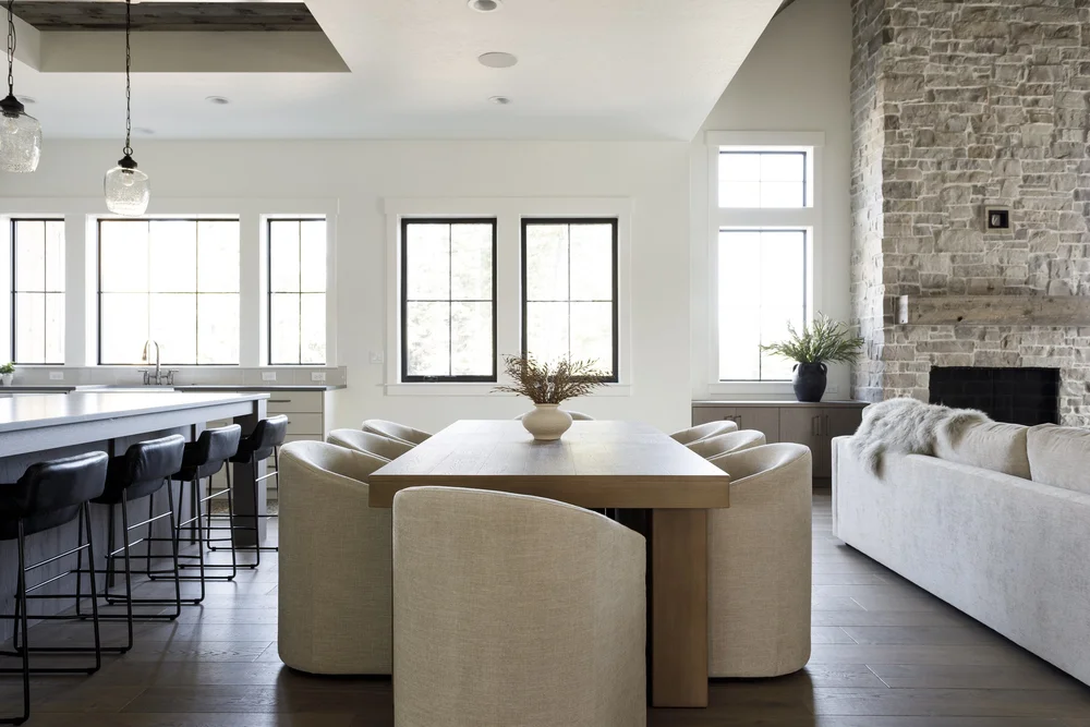 Bright open-plan dining area with wooden table, cream chairs, kitchen island, and stone fireplace