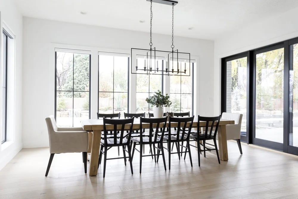 Bright modern dining room with wood table, black chairs, chandelier, and large black-framed windows