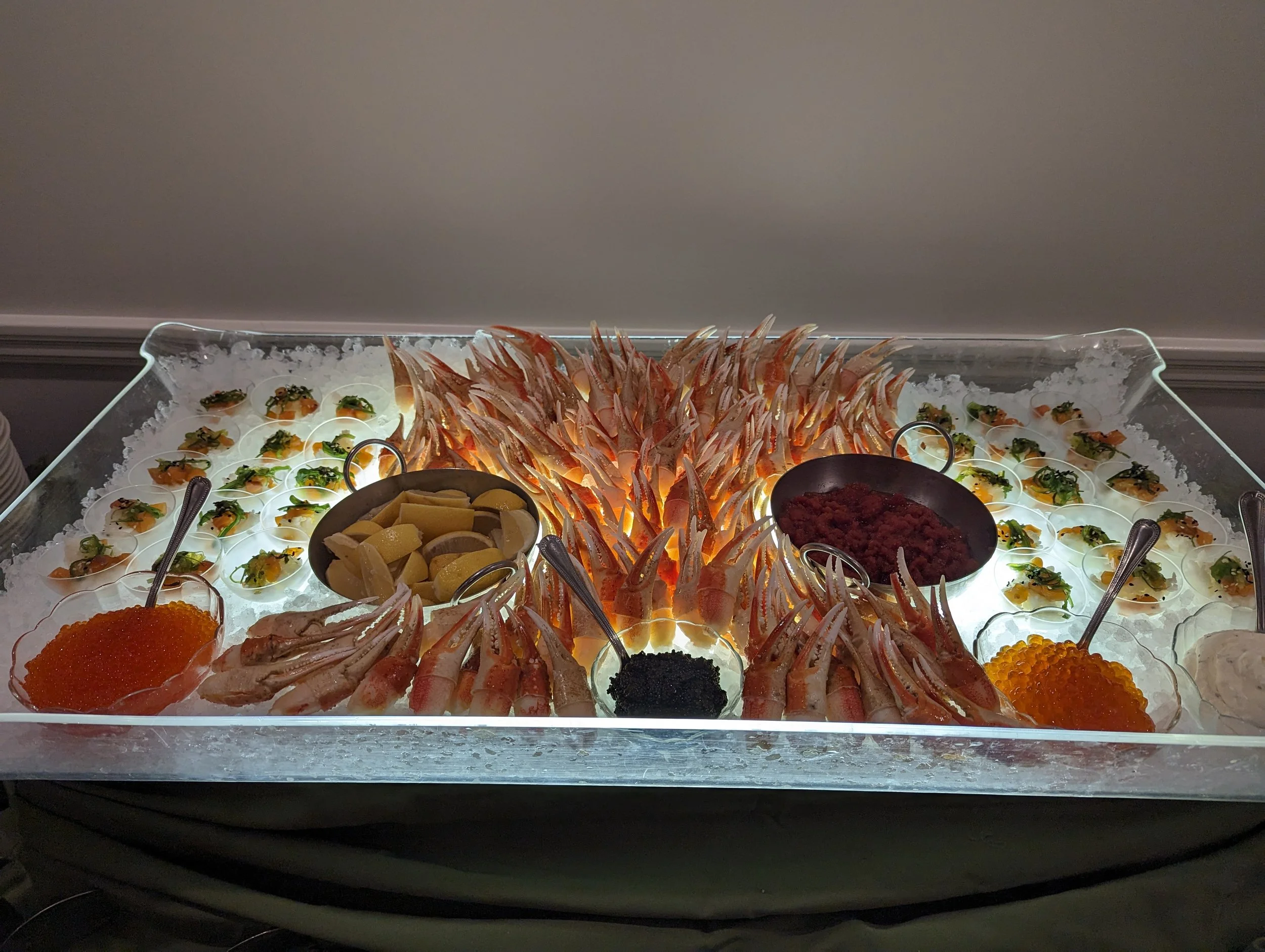 Seafood display on ice featuring shrimp, fish roe, shellfish, lemon wedges, and various condiments.