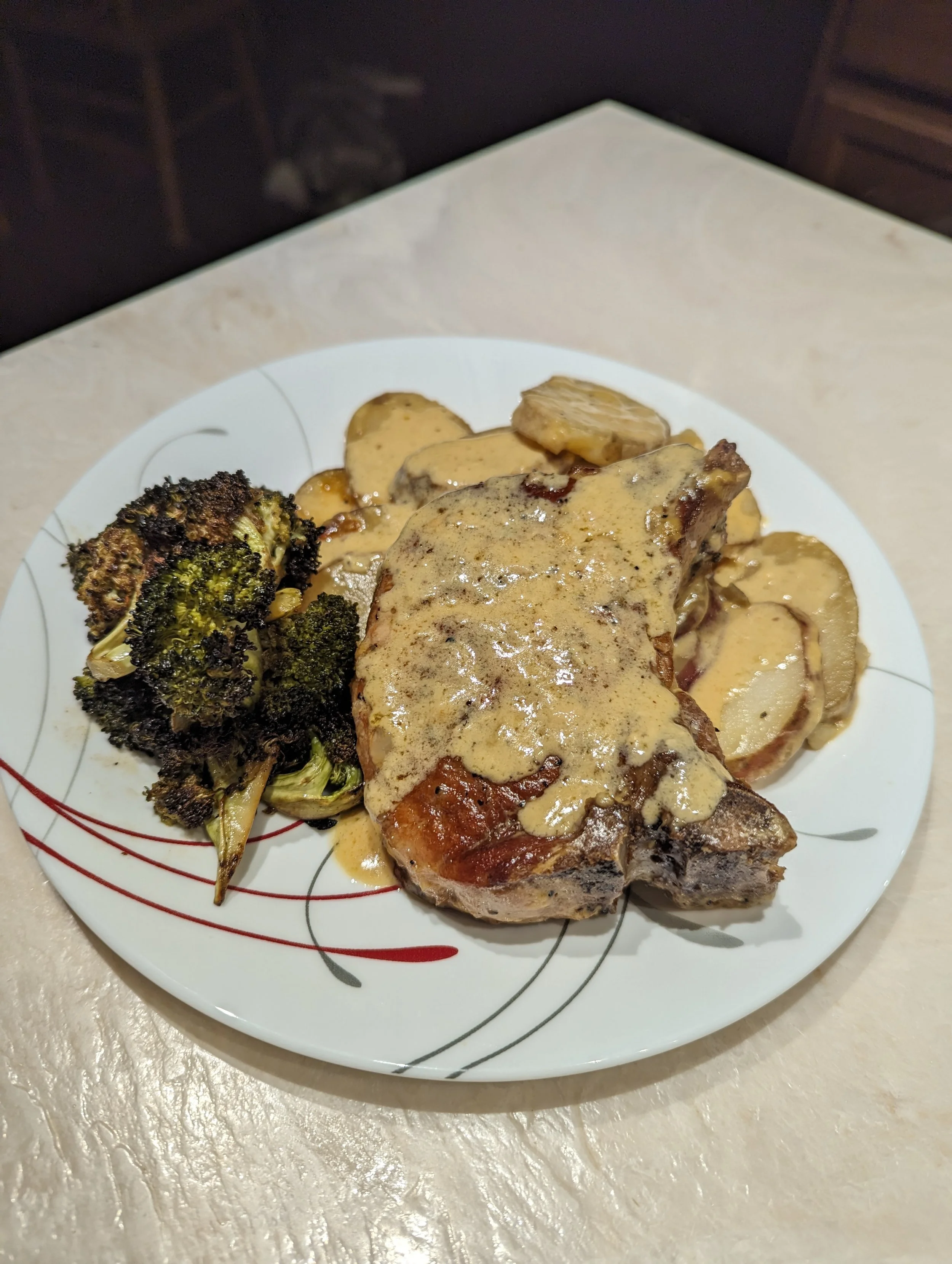 A plate with cooked broccoli florets, roasted potatoes, and a pork chop topped with a creamy mustard sauce.