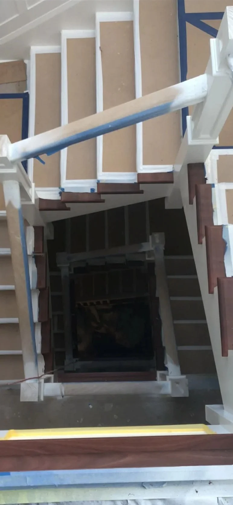 Top view of a staircase under construction, with partially installed white and dark wooden steps and a wooden handrail.