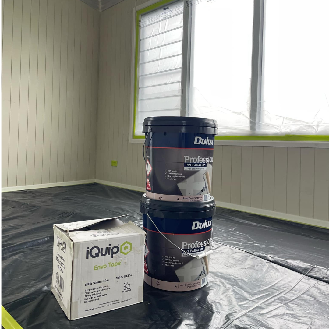 Two large buckets of Dulux professional acrylic sealer primer in a room with plastic covering the floor, and a box of iQuip Envo Tape on the floor.