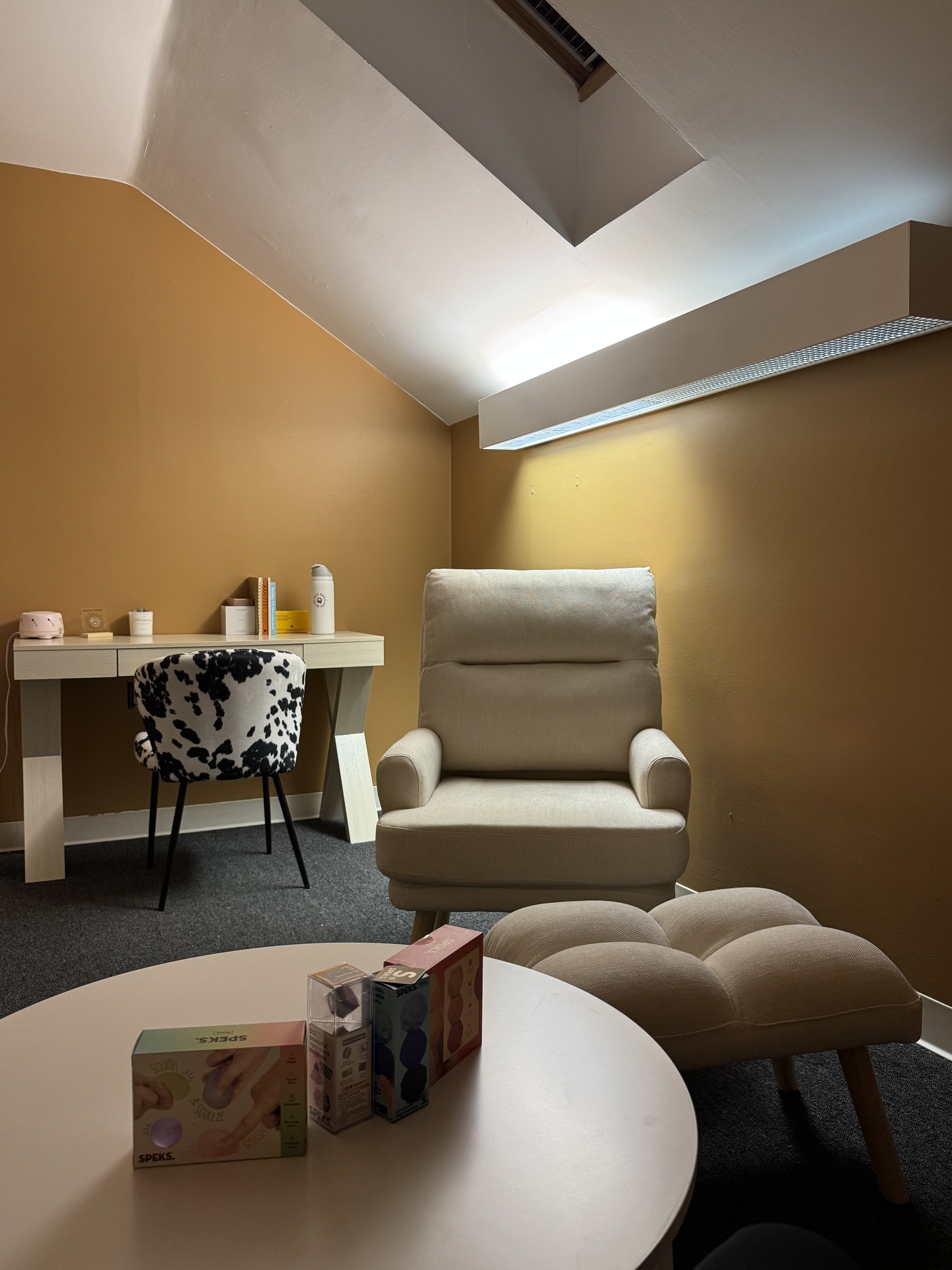Chair facing a small round table in the foreground, desk with chair in the background.