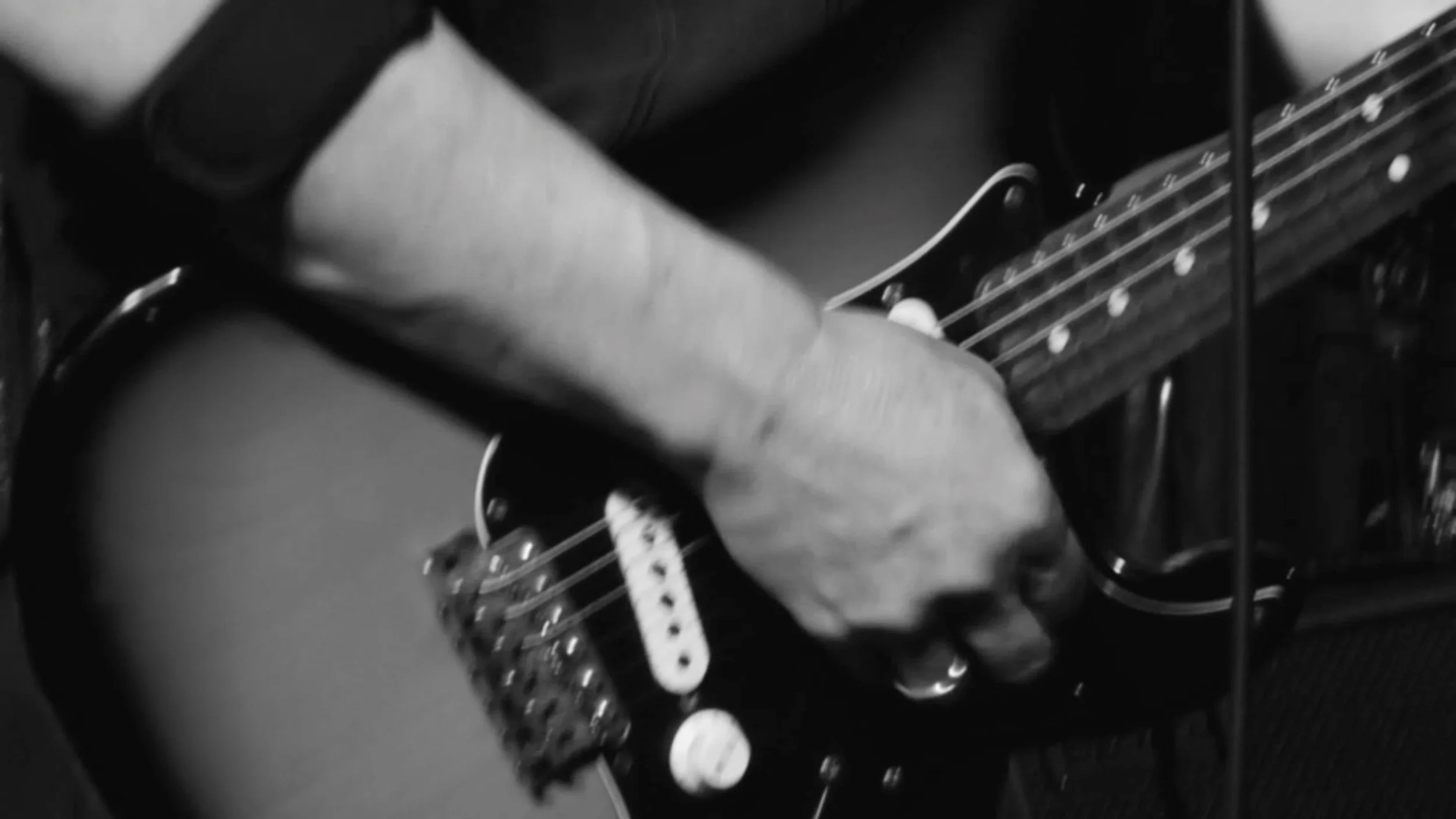 A person playing an electric guitar, with their hand on the fretboard, in black and white.