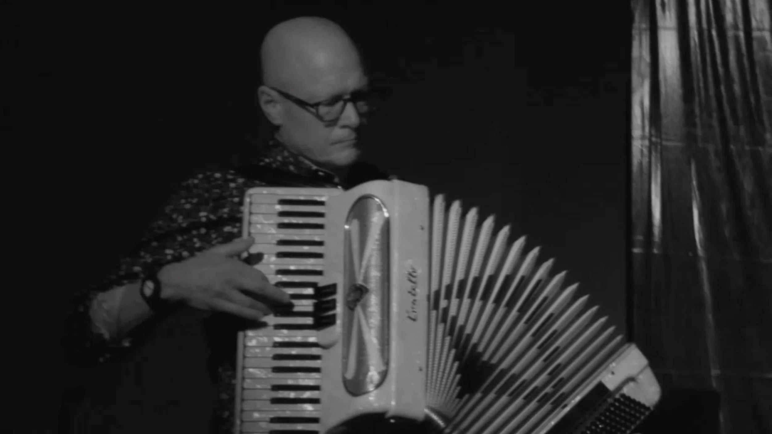A man with glasses and a bald head playing an accordion.