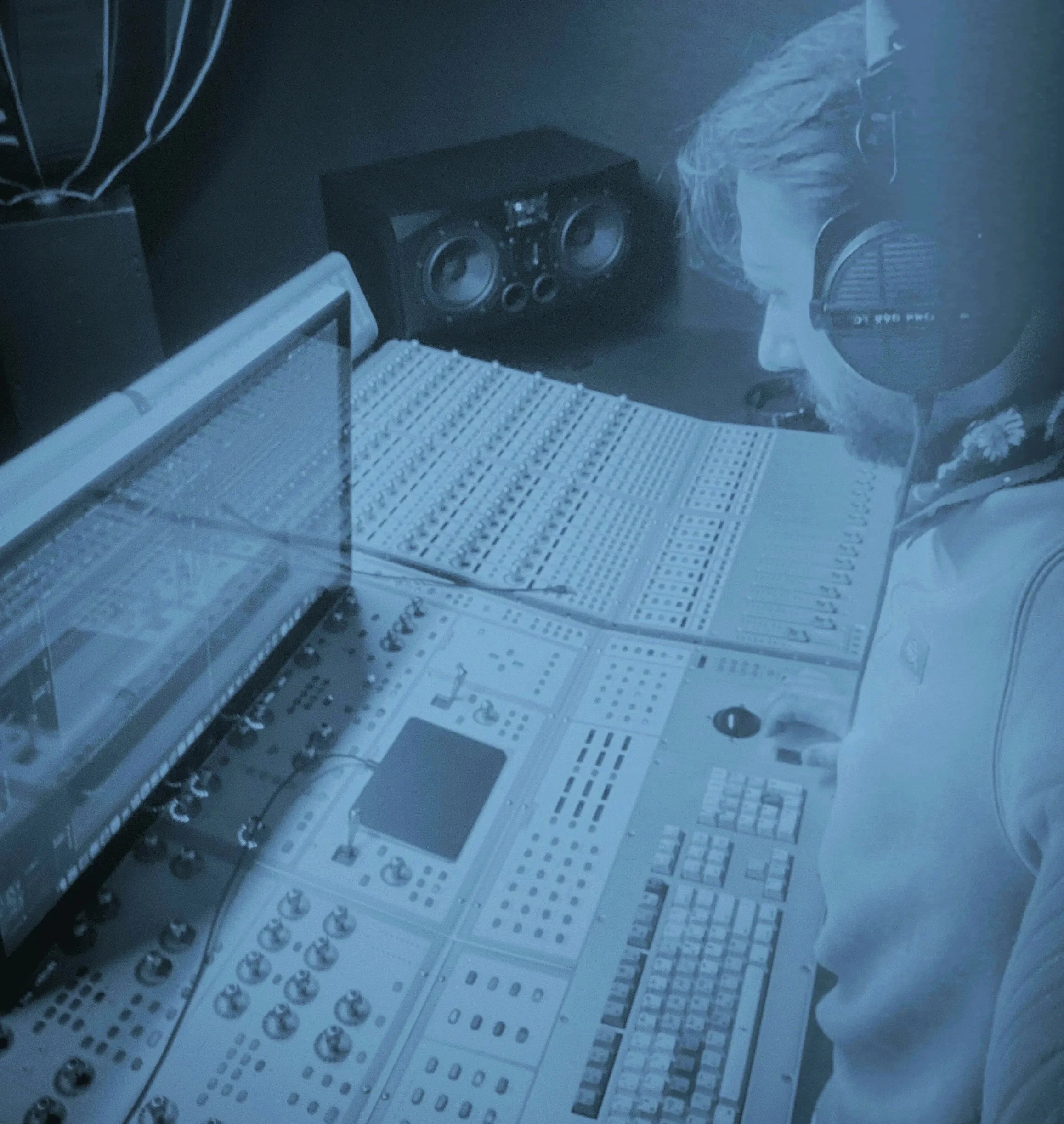 Un homme avec des écouteurs dans un studio d'enregistrement, regardant un panneau de contrôle avec plusieurs écrans et équipements audio.