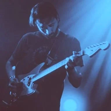Musicien jouant de la guitare électrique sur scène avec une lumière bleue