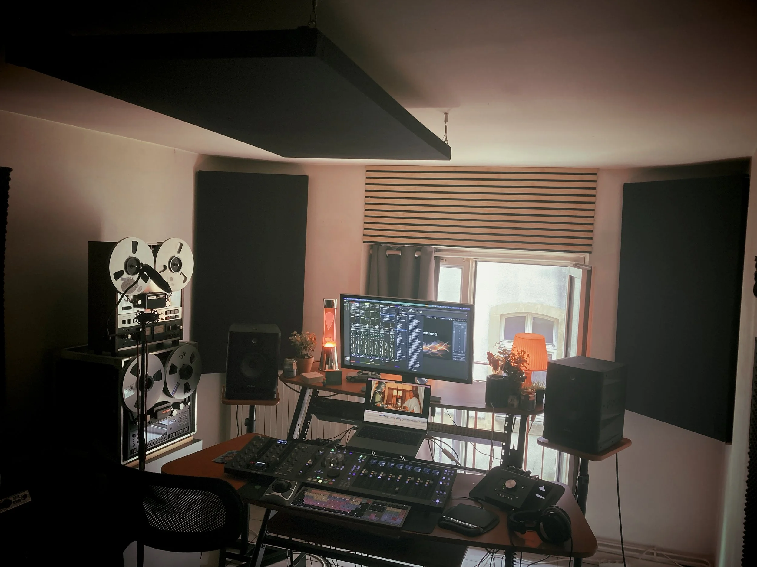 Studio de musique avec équipement audio, écran de contrôle, deux haut-parleurs, ordinateurs, lampe et plantes près de la fenêtre.