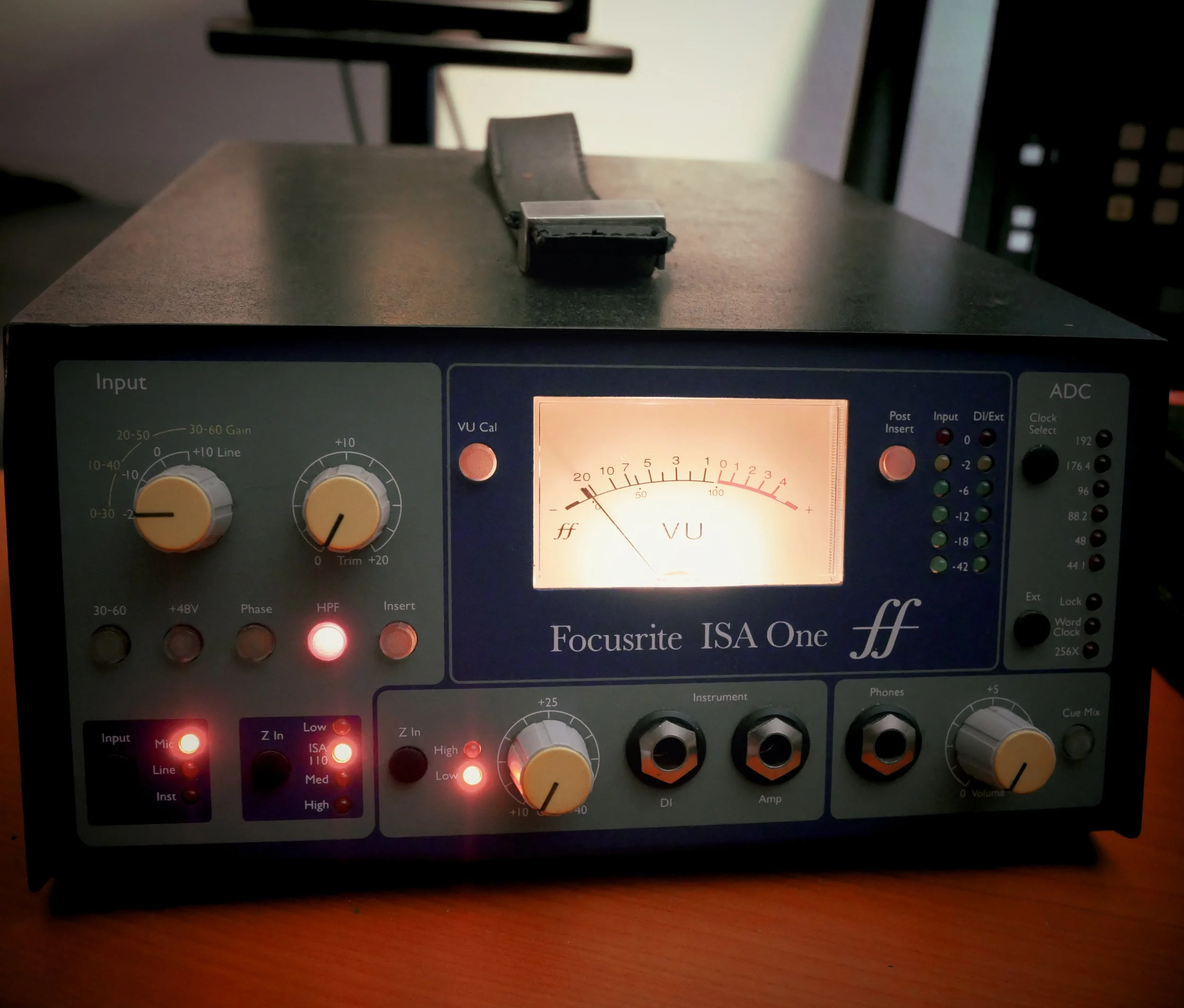 Un équipement de studio audio, un préamplificateur et DI Focusrite ISA One, avec affichage analogique, boutons de contrôle, et connecteurs pour microphones et instruments, allumé avec des indicateurs lumineux.