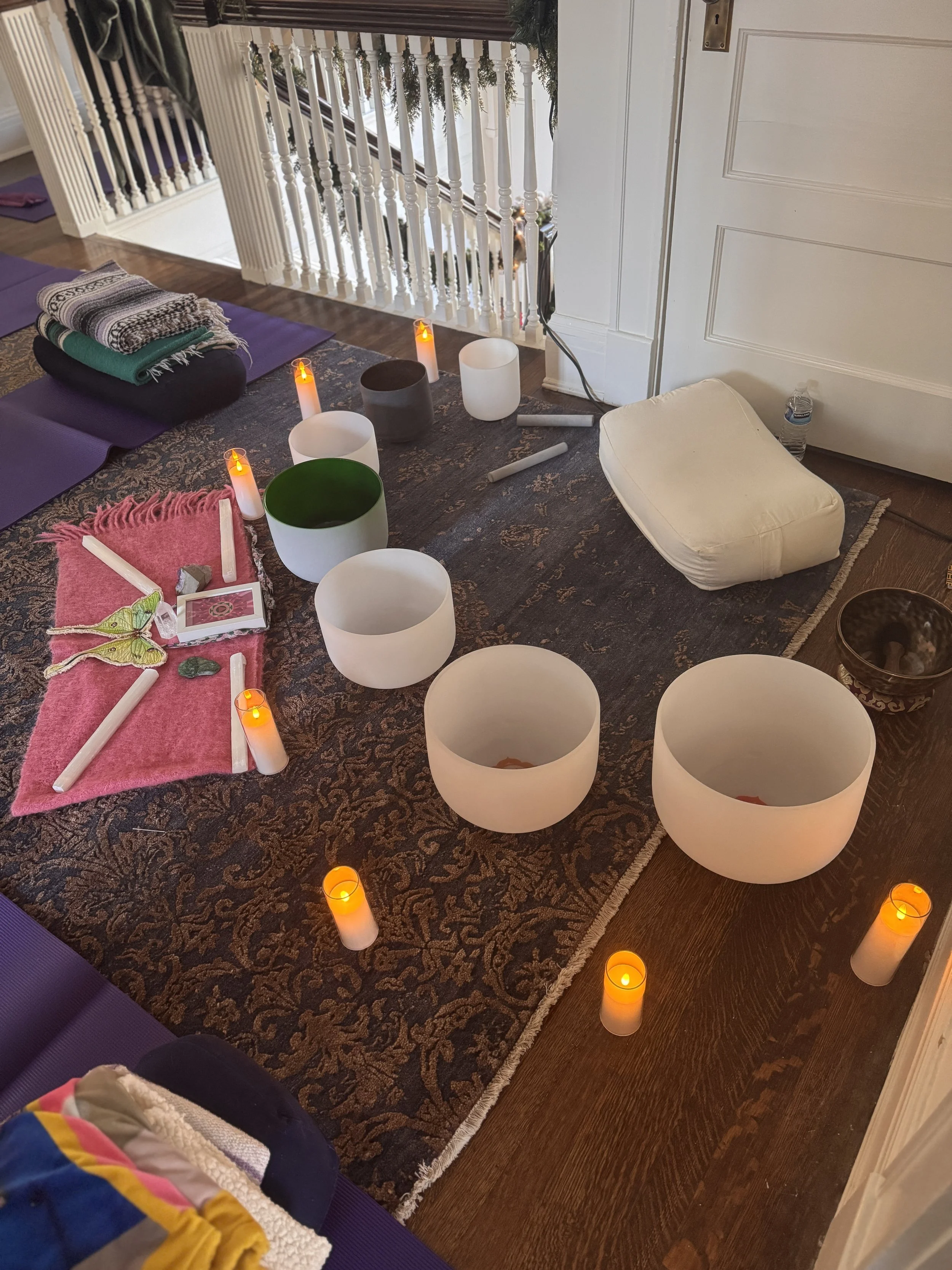 A cozy indoor space with musical instruments and candles arranged for meditation or relaxation. Includes singing bowls, candles, a pillow, and yoga mats.