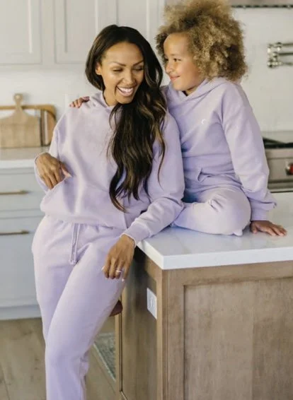 Mother and daughter laughing and smiling in matching lavender loungewear in a modern kitchen.