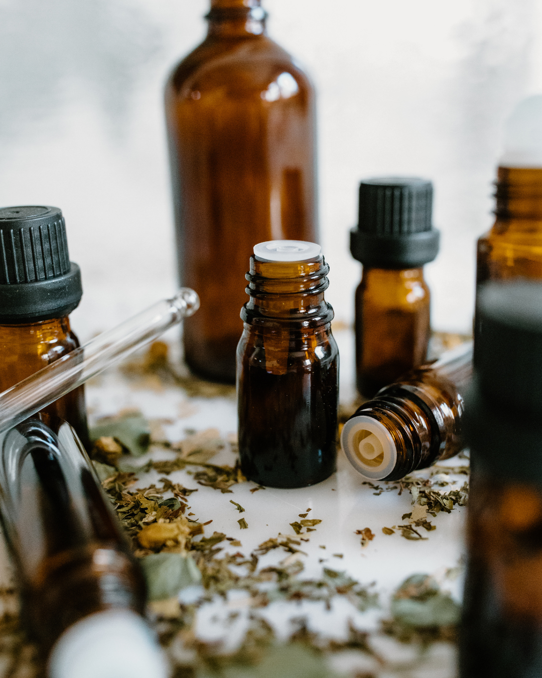 Amber glass essential oil bottles with dried herbs on a white surface
