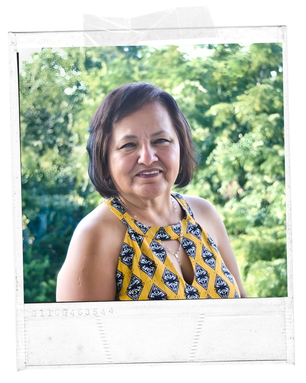 Portrait of a middle-aged woman with dark brown hair and a yellow and black patterned sleeveless top, outdoors with green foliage in the background.