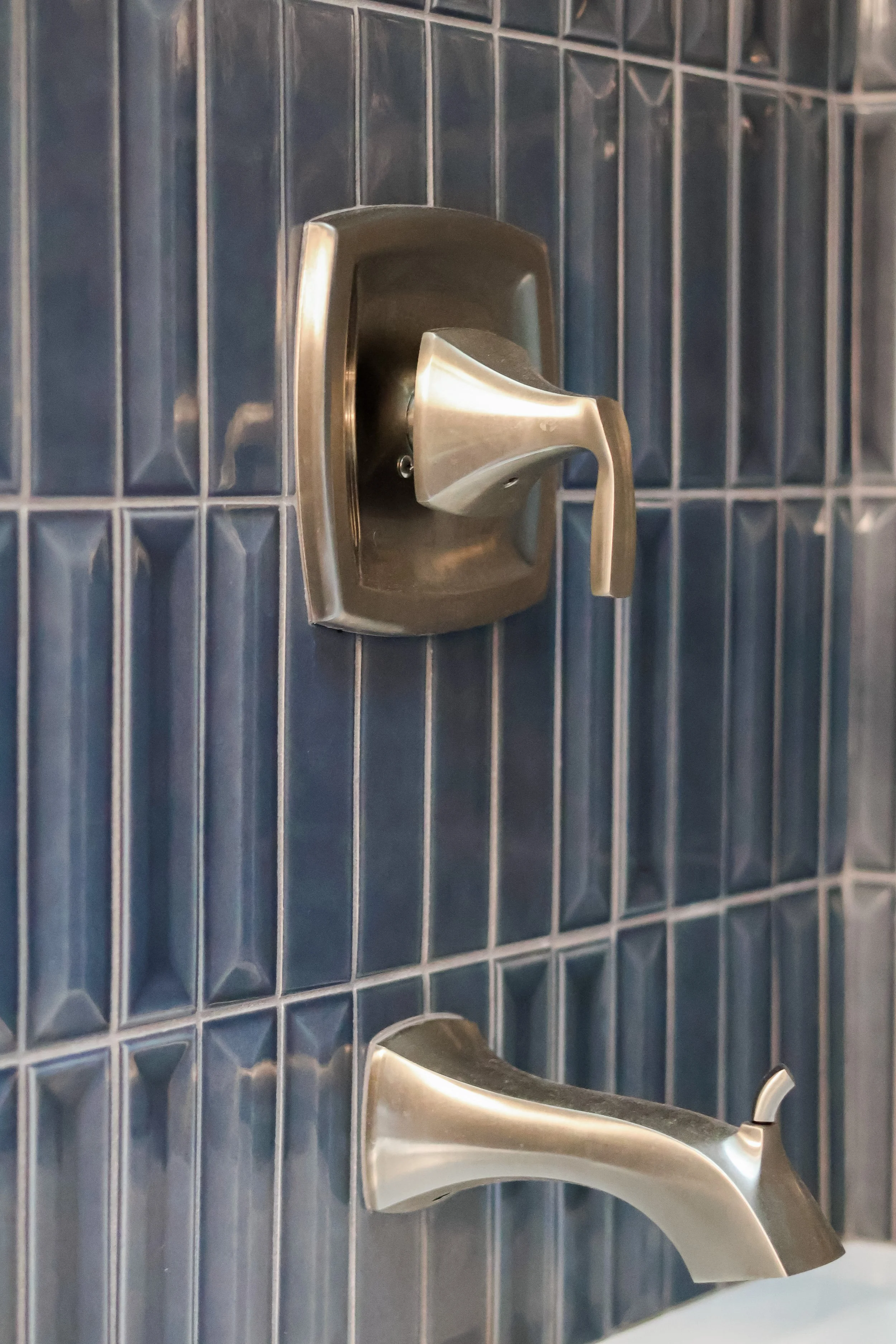 Close-up of a stainless steel faucet mounted on a tiled bathroom wall.