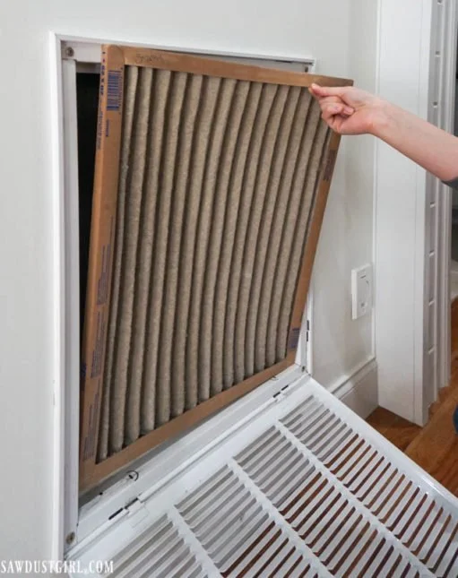 Person removing a dirty air filter from a vent in a wall.