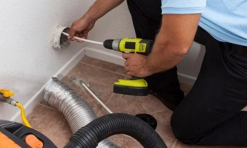 Person using a screwdriver on a wall with a flexible pipe nearby.